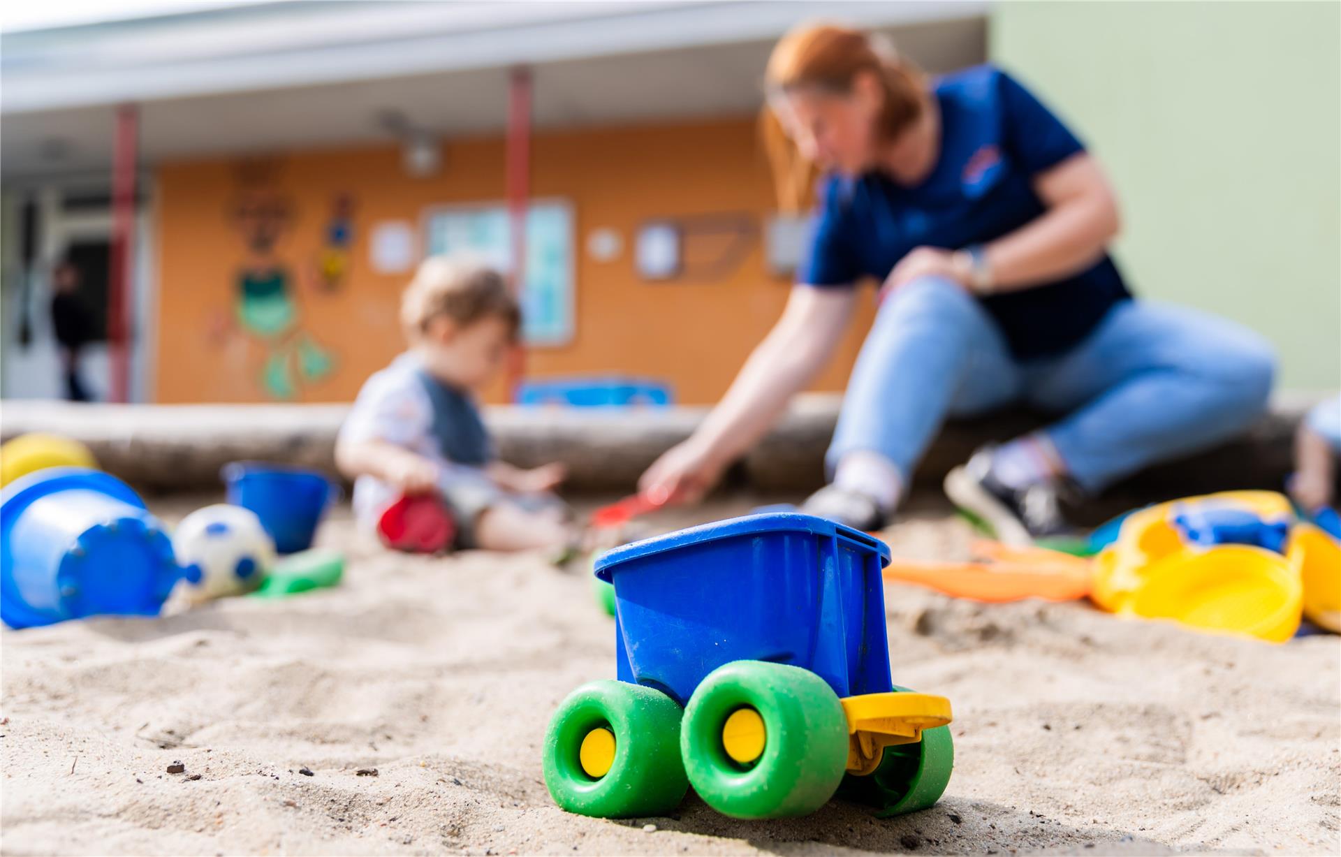 Ein Kind spielt mit einer Erzieherin im Sandkasten einer Kita.