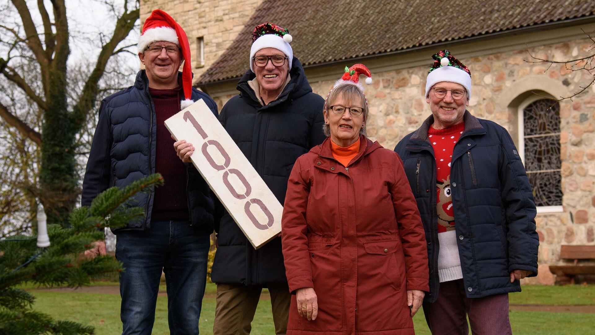 3 Männer und eine Frau lachen in die Kamera. Alle haben Weihnachtsmützen auf. 