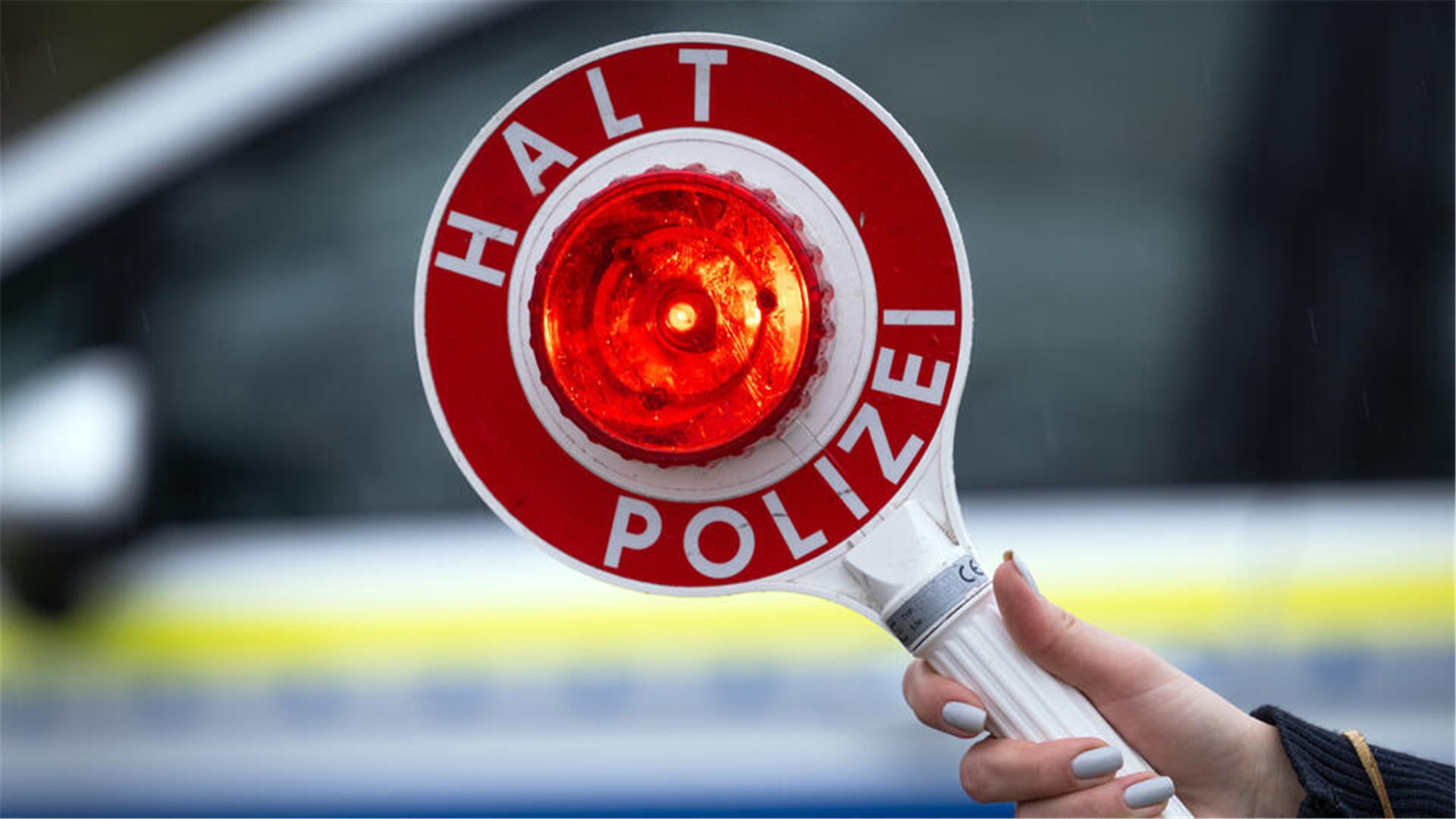 Eine Polizistin hält während einer Verkehrskontrolle eine Polizeikelle mit der Aufschrift "Halt Polizei".