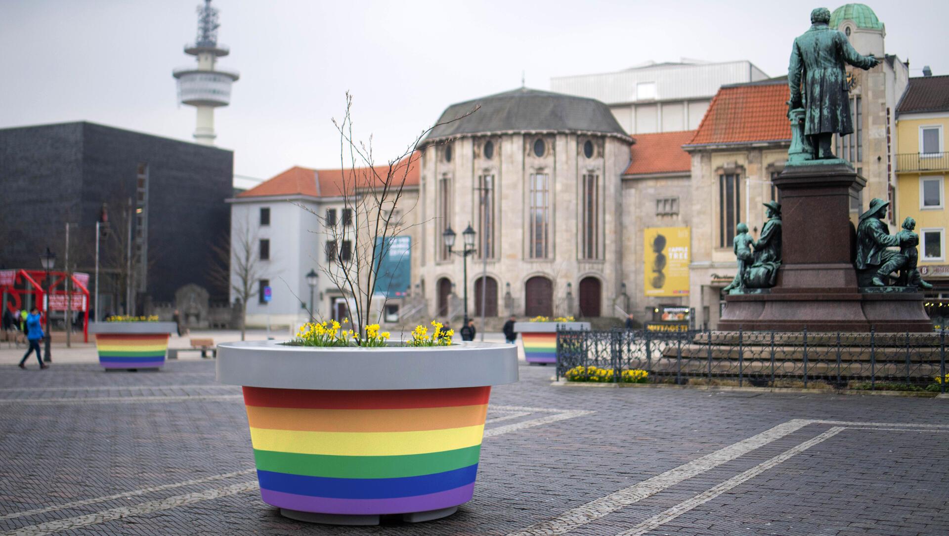 Ein Kübel in regenbogenfarben ist auf einem öffentlichen Platz zu sehen. 