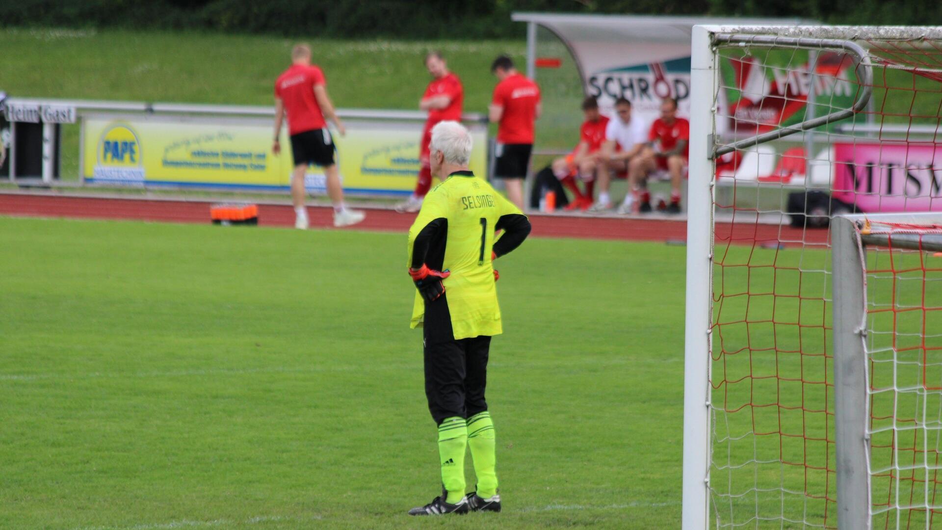 ein Mann in grünschwarzem Trikot steht mit dem Rücken zu einem Fußballtor