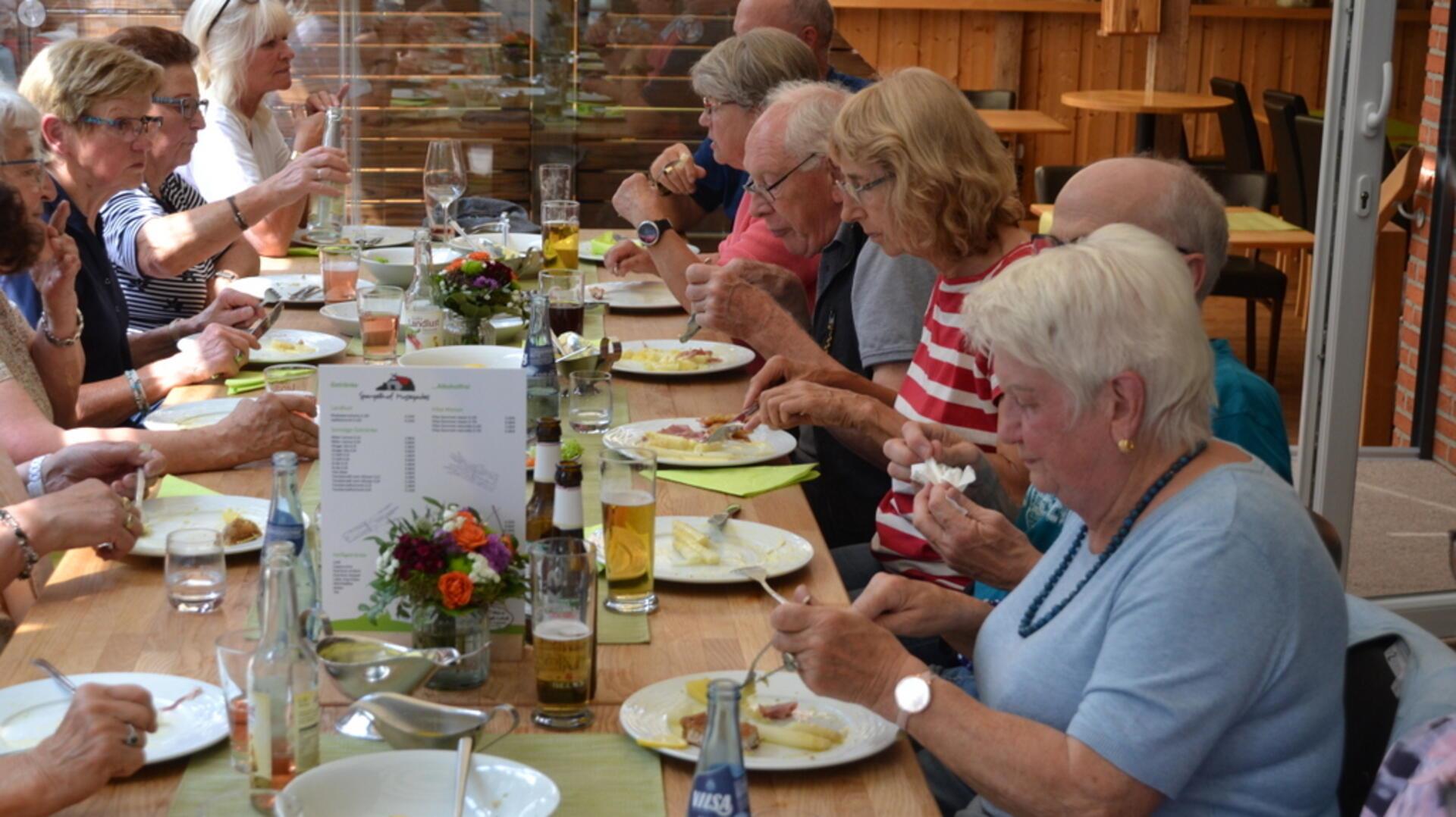 Leute sitzen an einem großen Tisch und essen Spargel. 