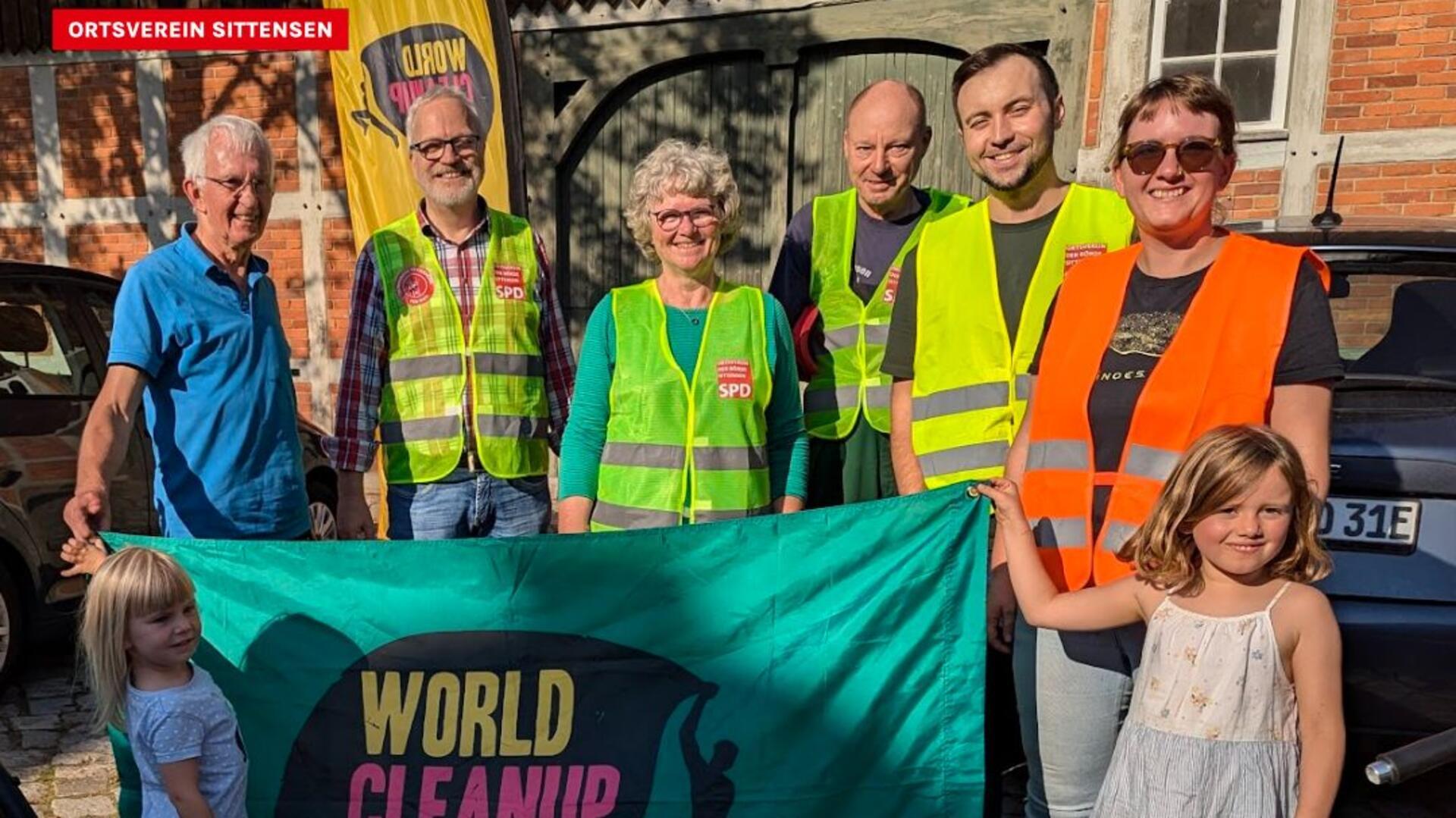 Einige Männer, Frauen und Kinder stehen nebeneinander und halten ein Transparent zum „World Cleanup Day“