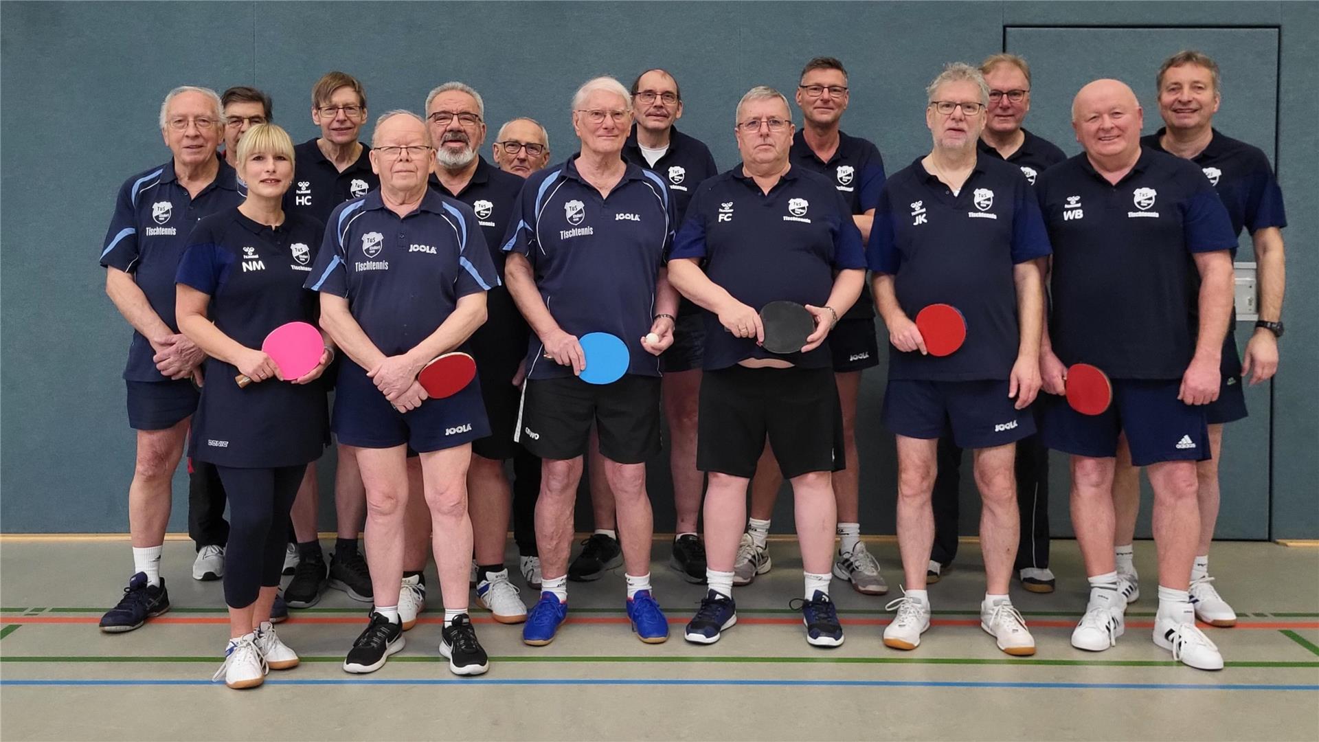 Viele Männer und eine Frau in dunklen Sporttrikots stehen in zwei Reihen.