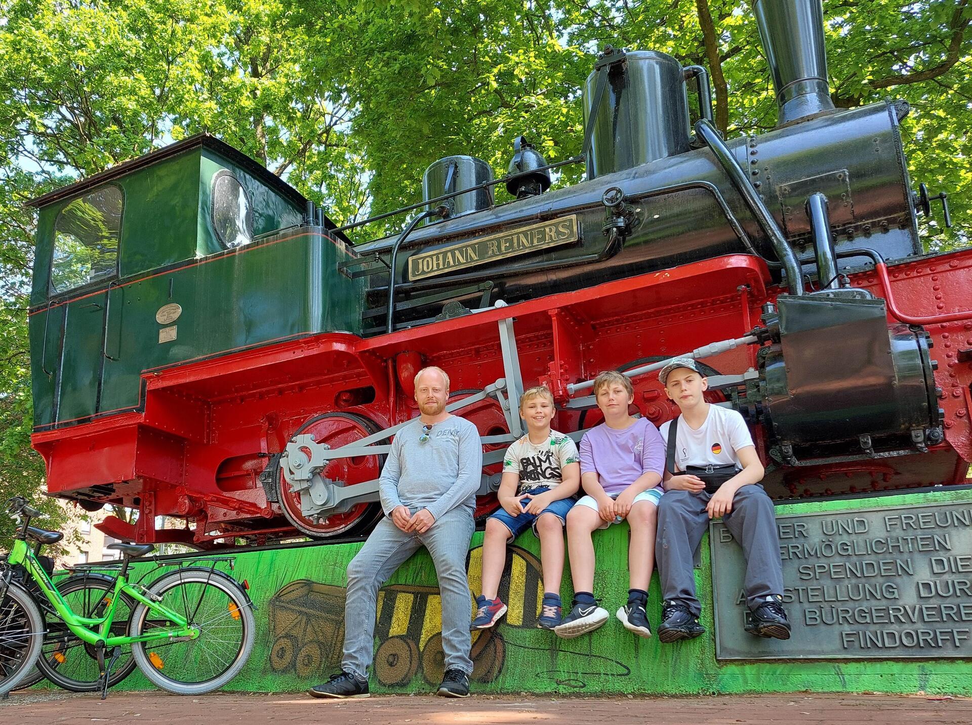 Die Stadtteilforscher Daniel Sokolis mit seinen Söhnen Ben (10), Louis (12) und Paul (14) (v.l.) vor der Denkmallok „Jan Reiners“ in Bremen-Findorff.