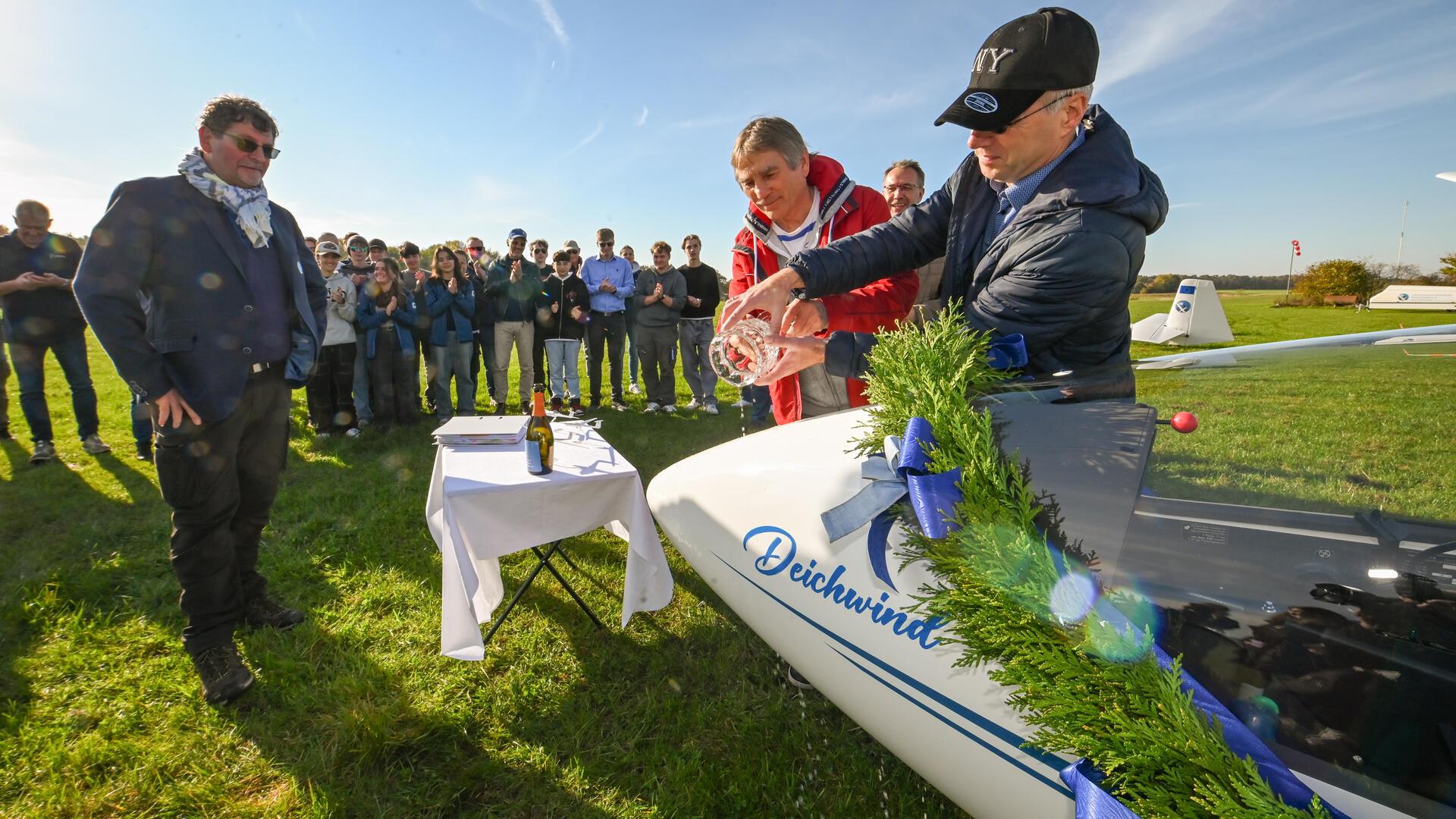 Der Luftfahrtverein Unterweser tauft sein neues Segelflugzeug auf den Namen „Deichwind“. Es gießen Stefan Axmann (rechts) und Jens Ennen unter Beobachtung von Hansjörg Kiesling (links) und Ralf Holz (hinten).