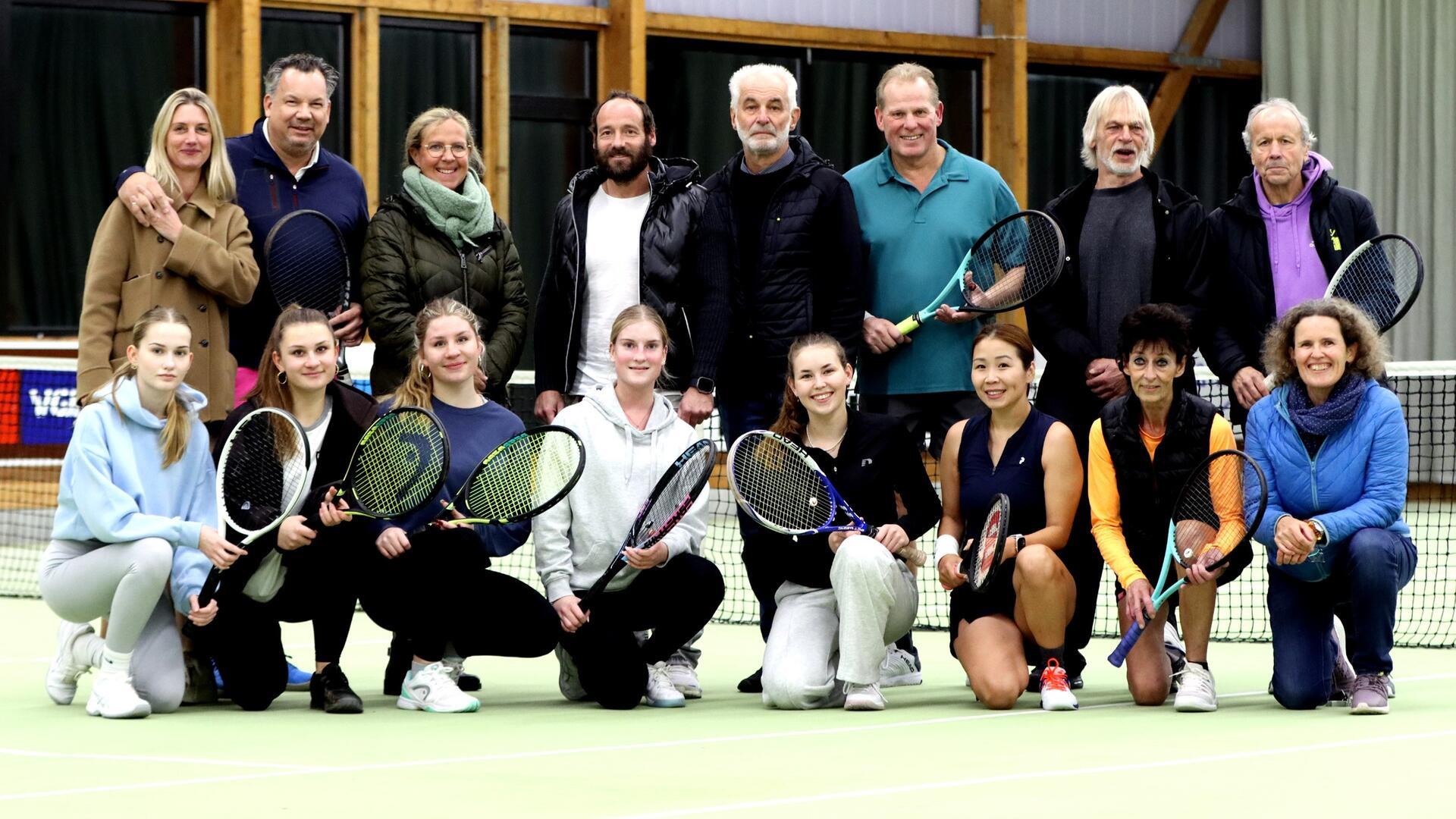 16 Männer und Frauen verschiedenen Alters, die teilweise Tennisschläger in der halten, stehen und hocken in zwei reihen.