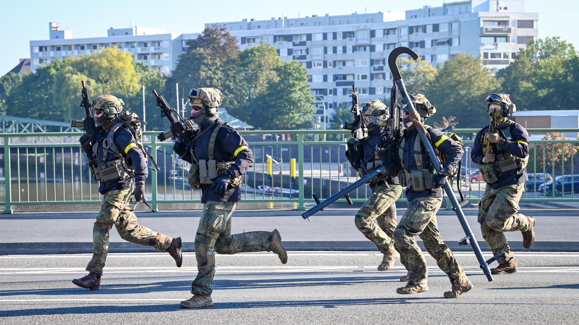 Fünf vermummte und mit Waffen ausgerüstete Männer rennen. 