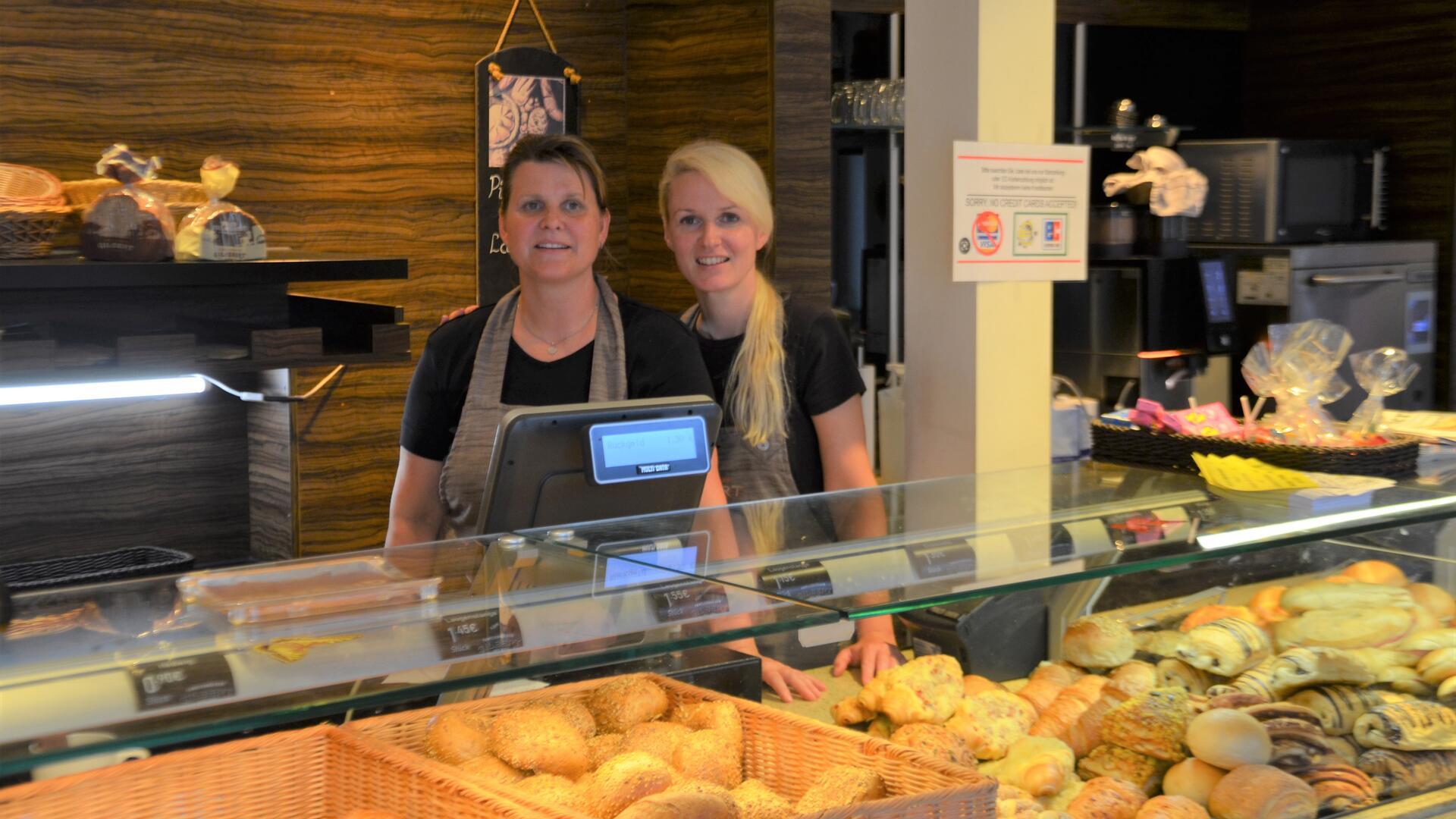 Zwei Frauen stehen hinter dem Bäckertresen und blicken in die Kamera. 