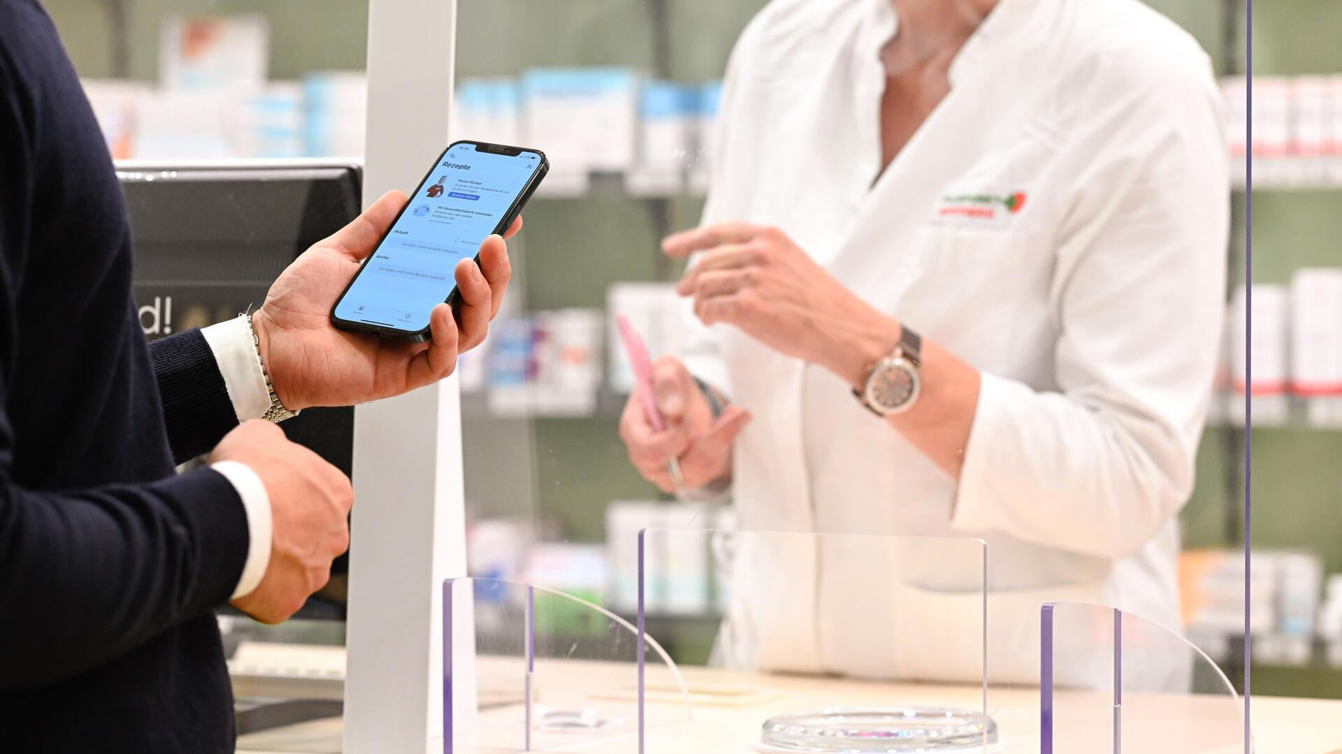 Ein Mann steht mit Handy in einer Apotheke. Die ePA für alle soll auch eine Übersicht über alle Medikamente enthalten, die elektronisch verordnet und in der Apotheke ausgegeben wurden.