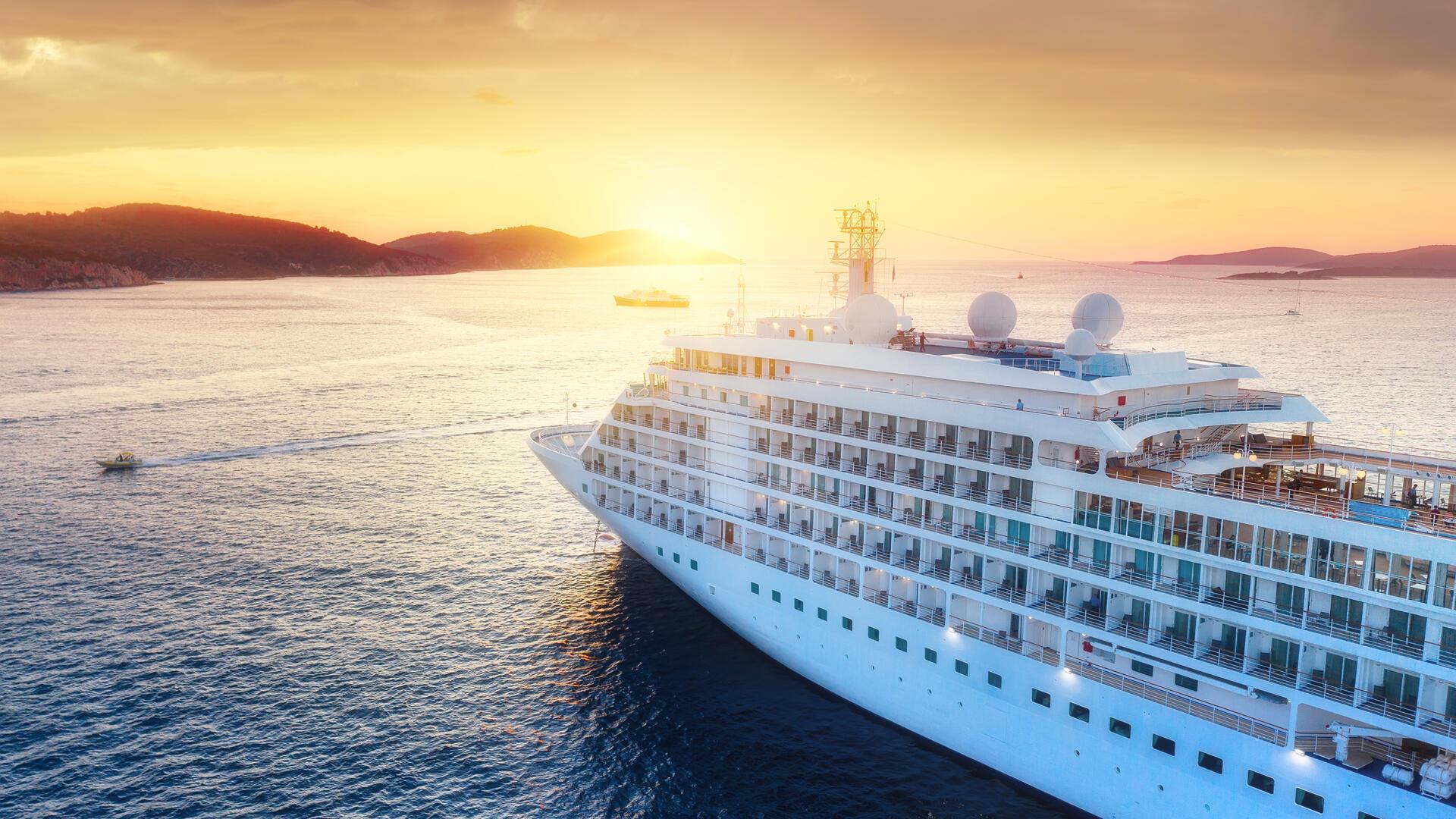 Ein Kreuzfahrtschiff fährt auf dem Meer vor einem Sonnenuntergang.