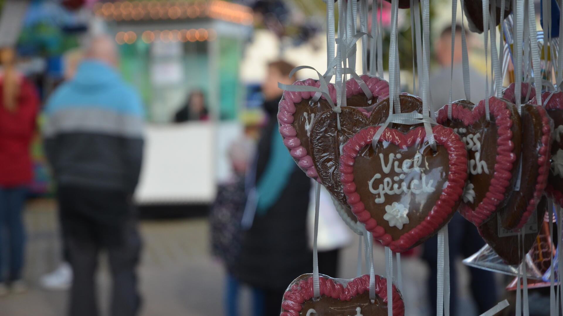 Lebkuchenherzen sind im Vordergrund. Im Hintergrund sind Menschen und ein Karussell. 