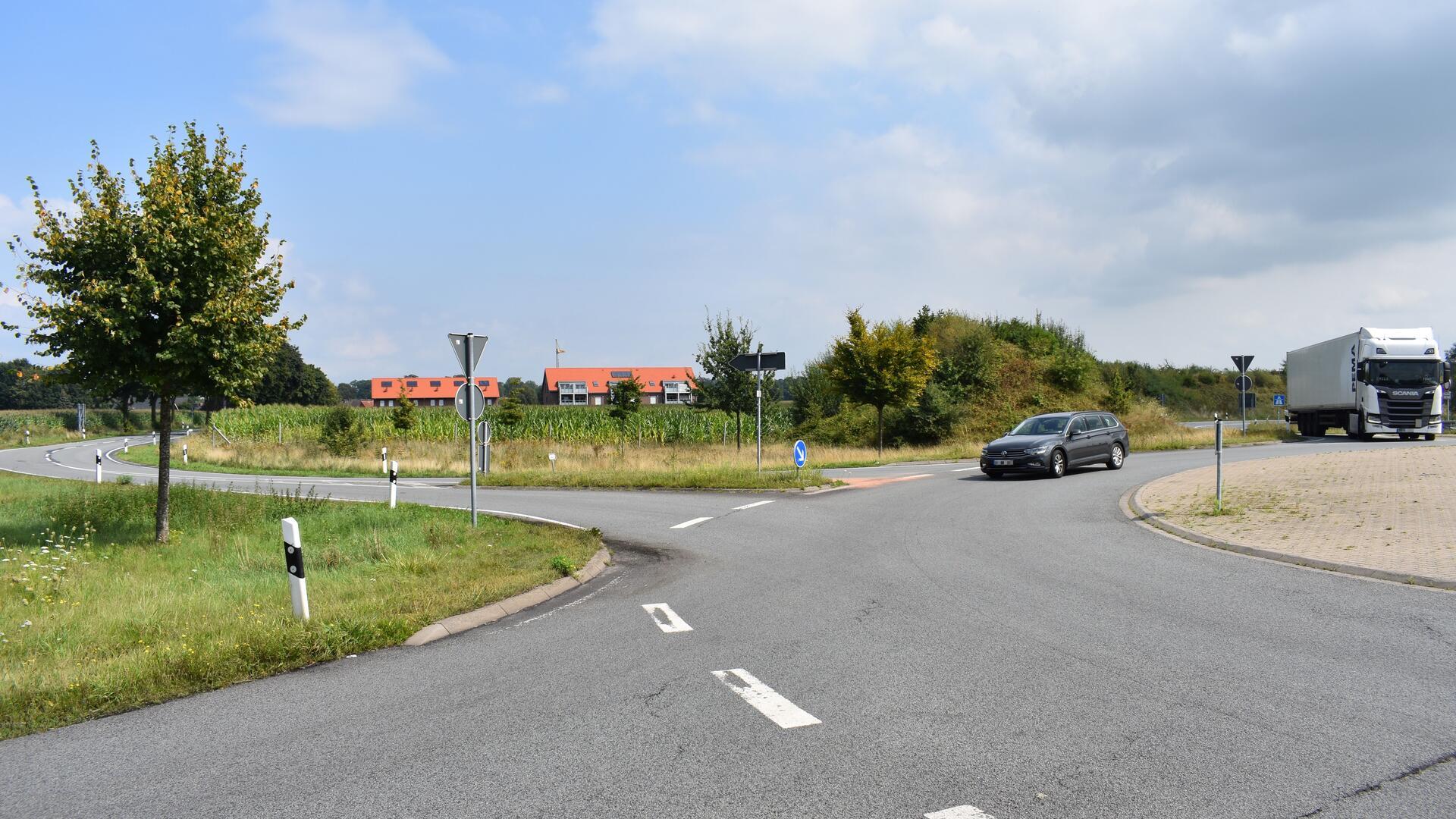 Eine Straße mit einem PKW und einem LKW, im Hintergrund ein Maisacker und die Dächer von zwei Mehrfamilienhäusern.