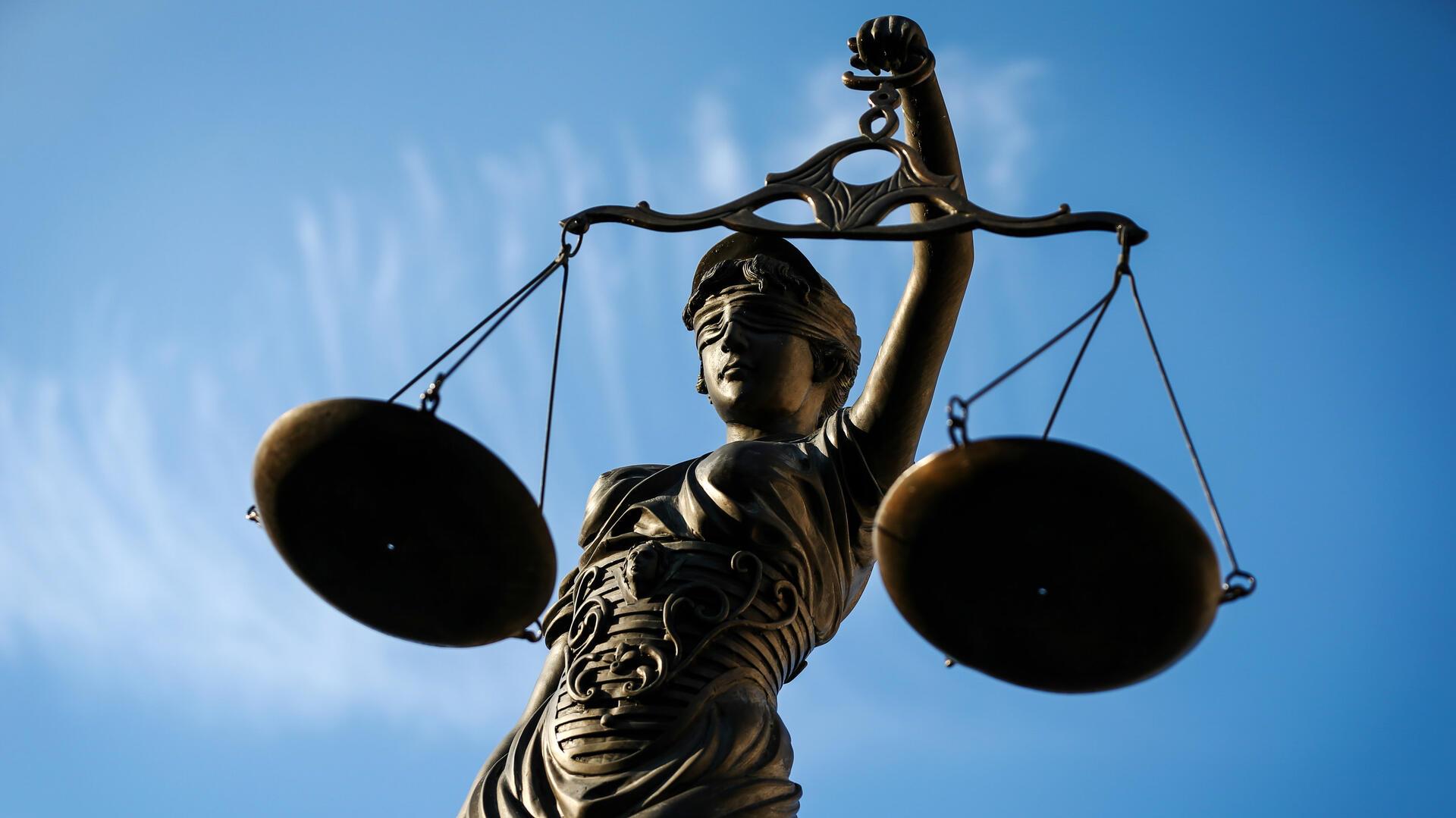 Nahaufnahme einer Statue der Justitia, der römischen Göttin der Gerechtigkeit, mit verbundenen Augen und einer Waage in der Hand, vor einem klaren blauen Himmel.