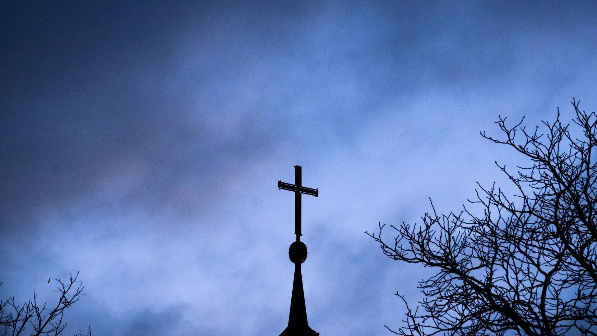 Dunkle Wolken ziehen über das Kreuz auf einer evangelischen Kirche in der Region Hannover.