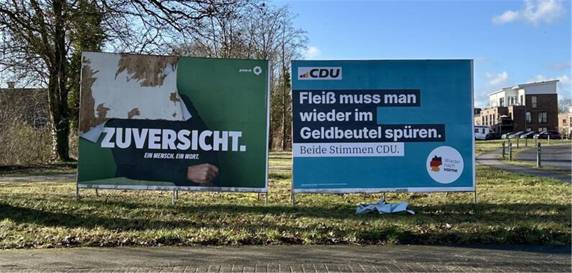 Zwei große Plakate stehen auf einer Wiese.