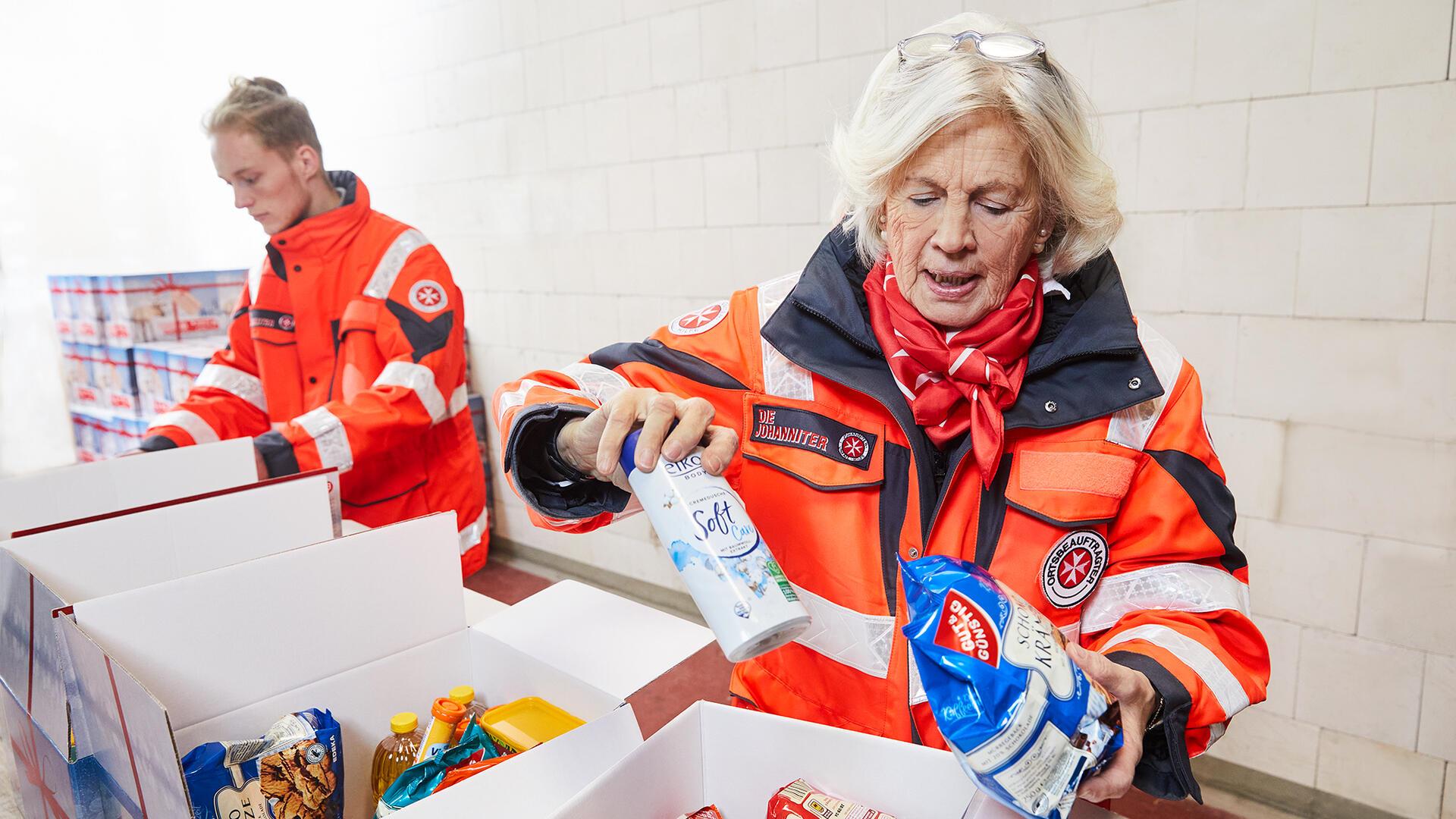 Ehrenamtlich Helfende der Johanniter befüllen Weihnachtstrucker-Pakete mit Lebensmitteln und Hygieneartikeln.