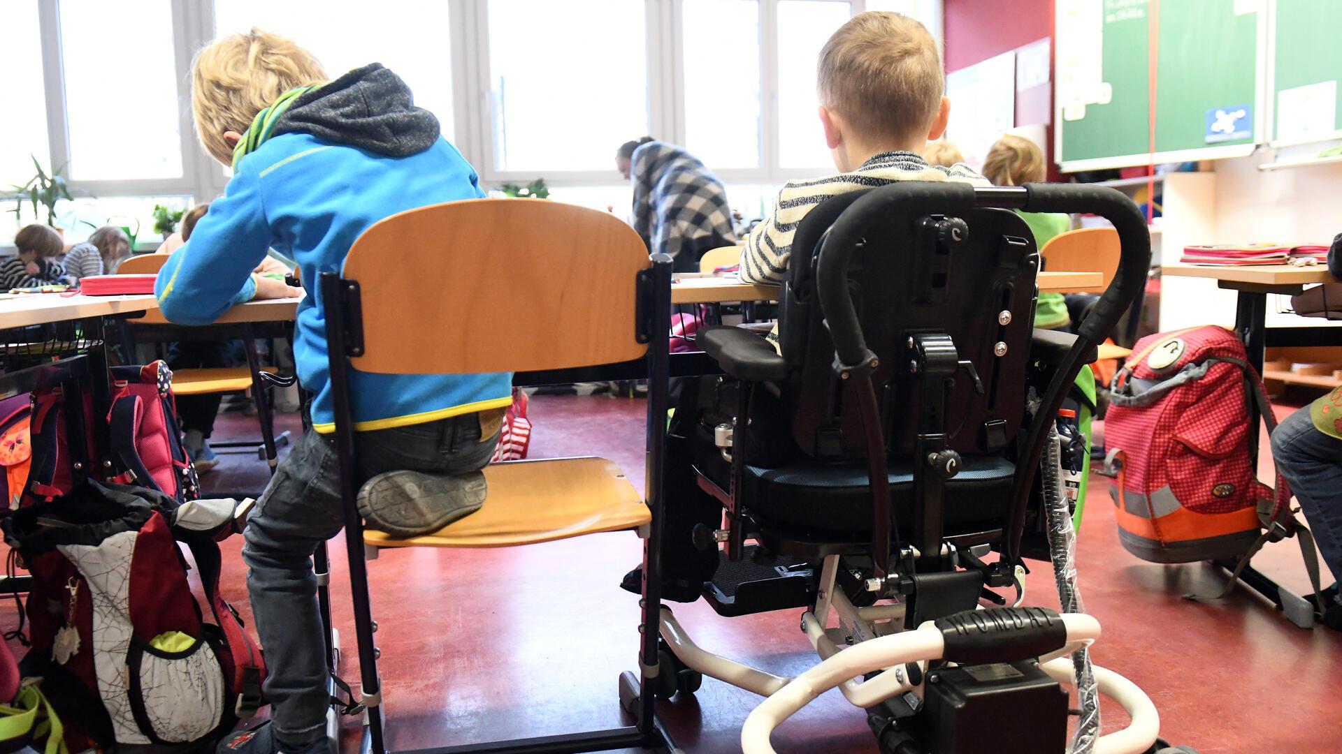 Ein Kind mit Behinderung sitzt in seinem Rollstuhl gemeinsam mit anderen Erstklässlern ohne Handicap in einem Klassenraum. 