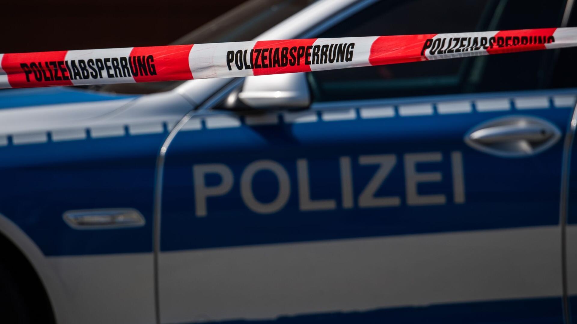 Ein Polizeiauto steht hinter einem Absperrband der Polizei.