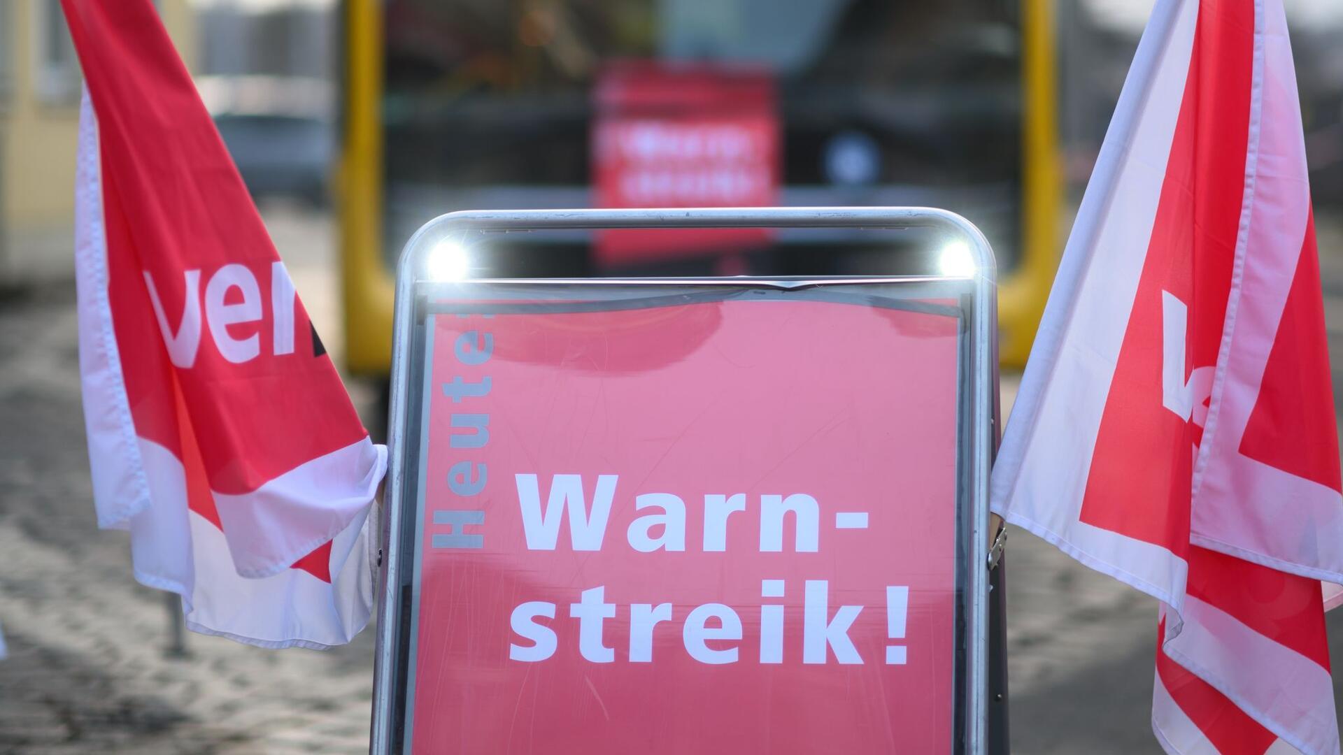 Ein Schild „Warnstreik“ steht vor einem Bus.