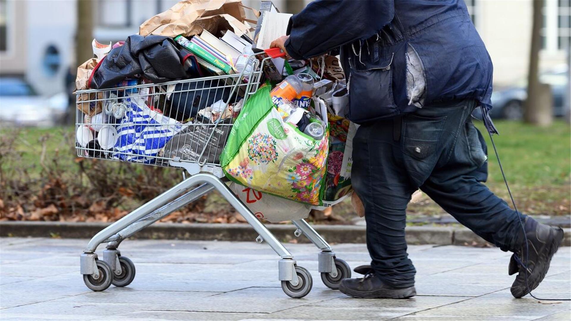  Ein obdachloser Mann schiebt einen Einkaufswagen über eine Fußgängerstraße. 