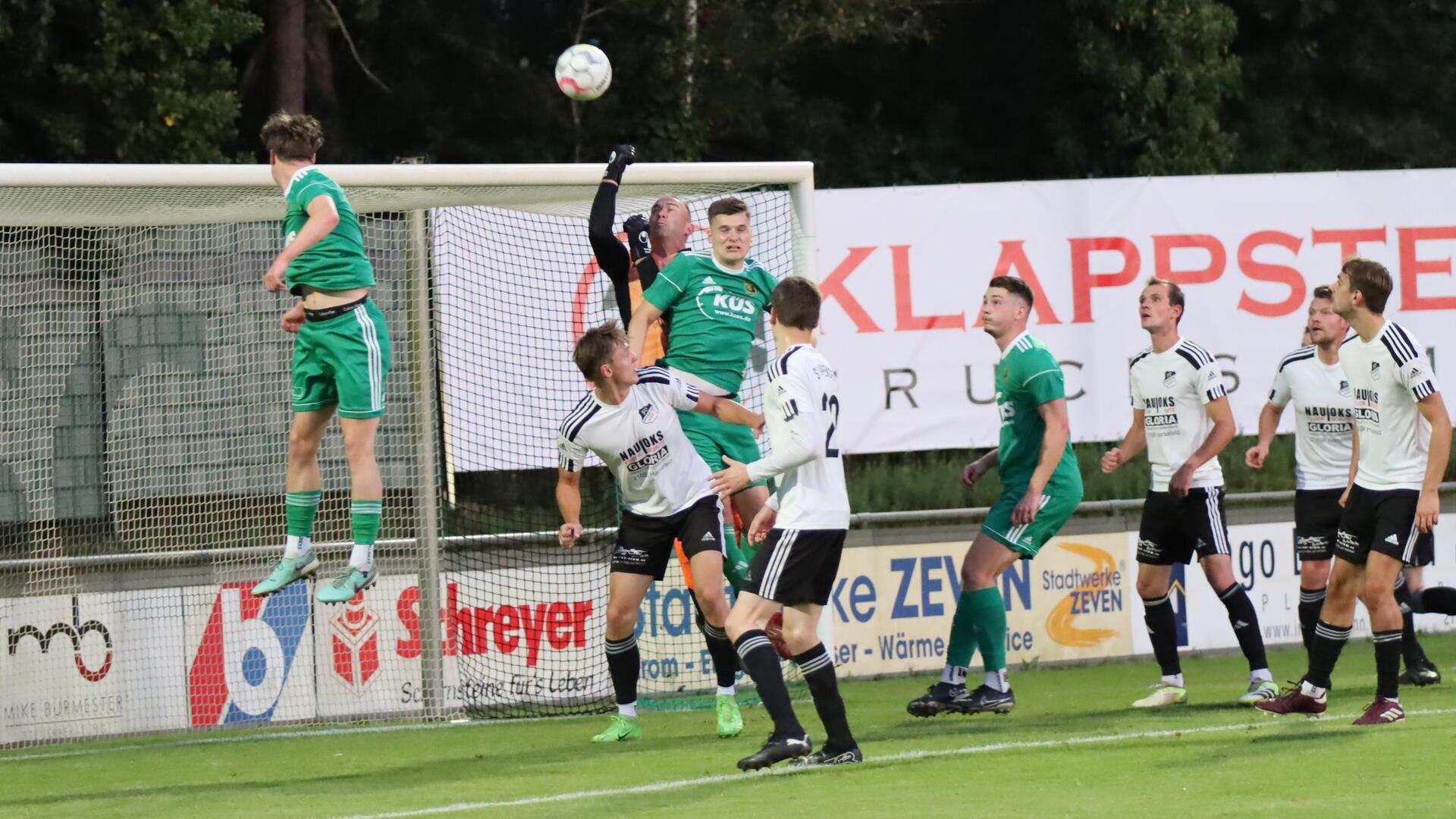 Männer in weißen und grünen Trikots vor einem Fußballtor.