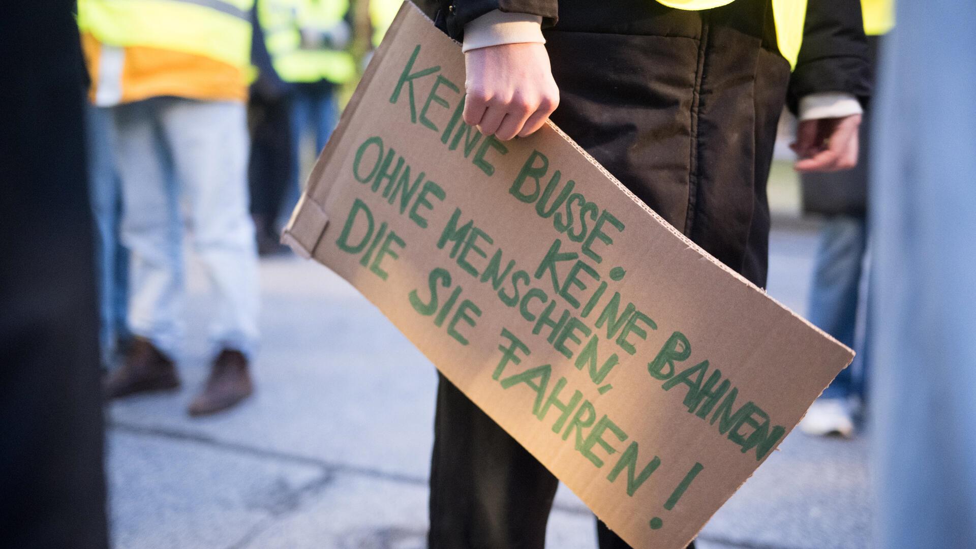 Eine Aktivistin von Fridays for Future, hält ein Schild mit der Aufschrift „Keine Busse, keine Bahnen, ohne Menschen, die sie fahren!“ in der Hand.