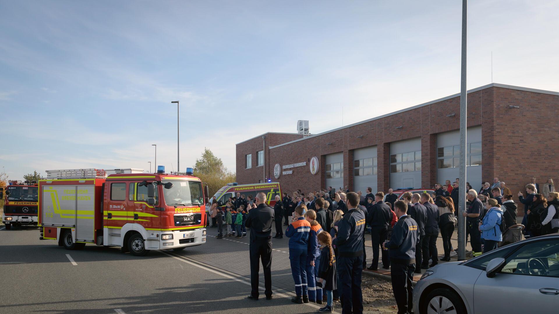 Menschen stehen vor einem Großen Gebäude, davor stehen Feuerwehrautos. 