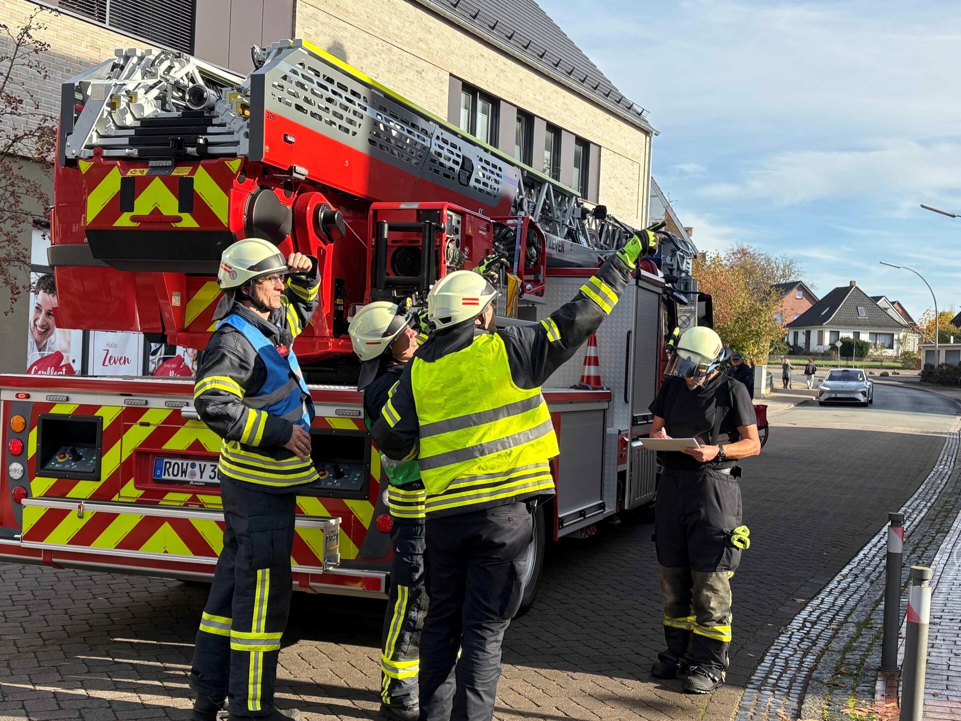 Vier Feuerwehrleute stehen vor einer Drehleiter. 