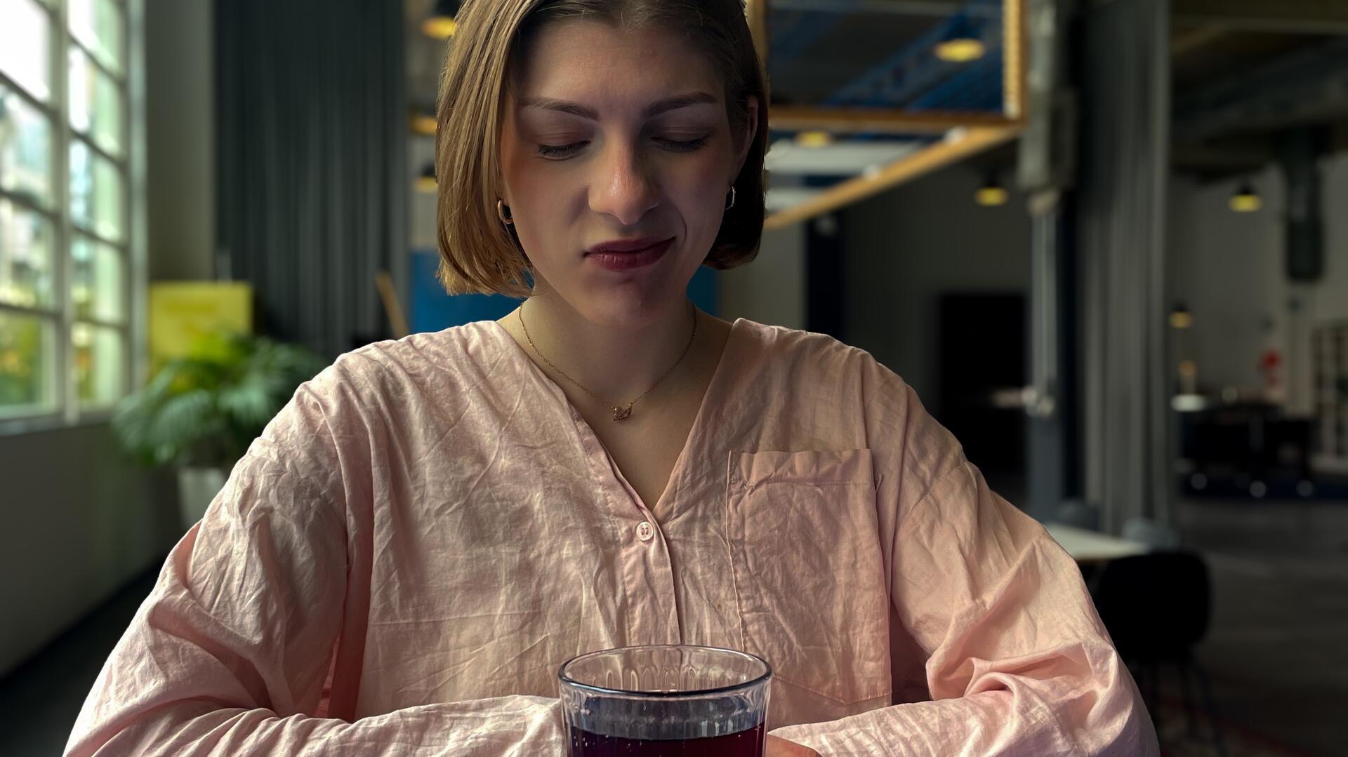 Eine Frau blickt skeptisch auf ein Glas mit Saft.