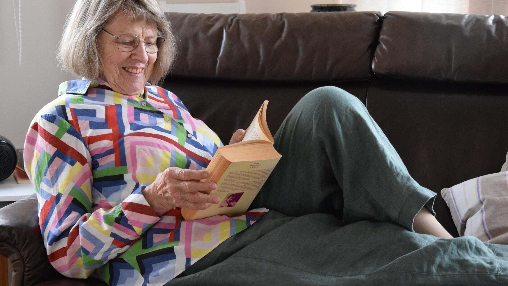 Eine Frau sitzt auf einer Couch und liest ein Buch.