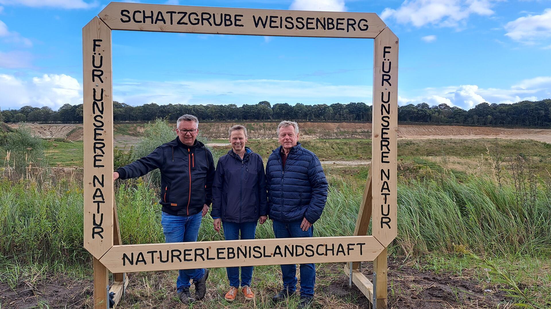 Bürgermeister Andreas Wittenberg (l.), Karla Mombeck von der BI MUT und Ortsbürgermeister Heinz Bühring weihen den neuen Fotorahmen an der Schatzgrube Weißenberg ein. 