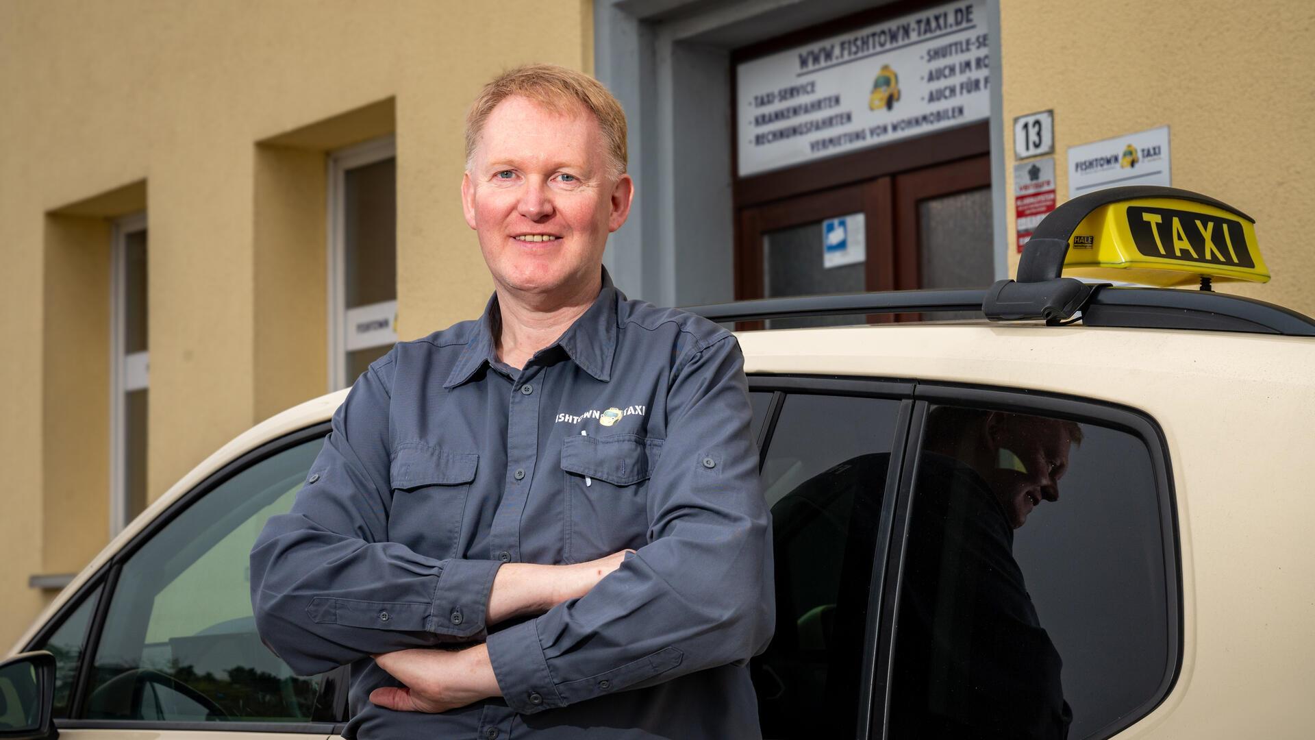 Ein Mann steht vor einem Taxi. 