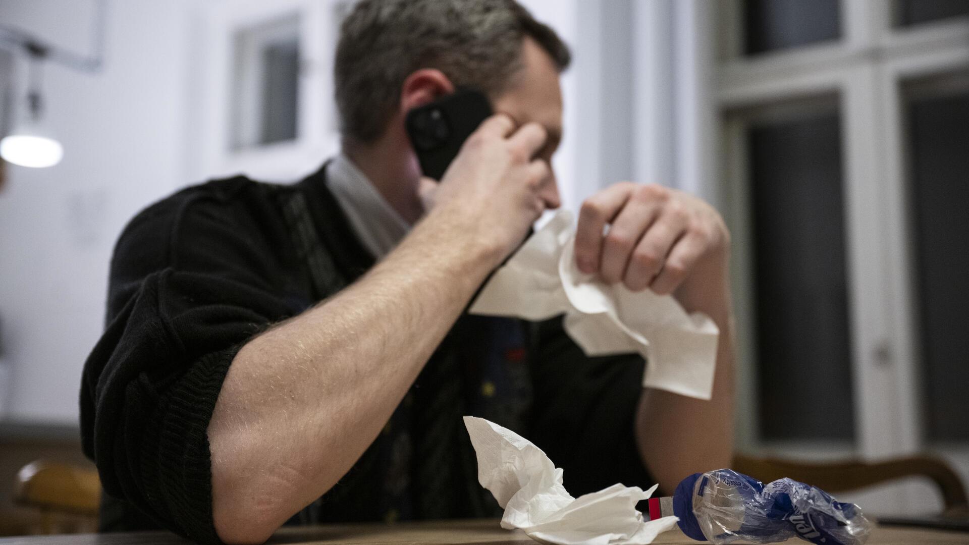 Ein Mann hält ein Taschentuch in einer Hand und ein Telefon in der anderen.