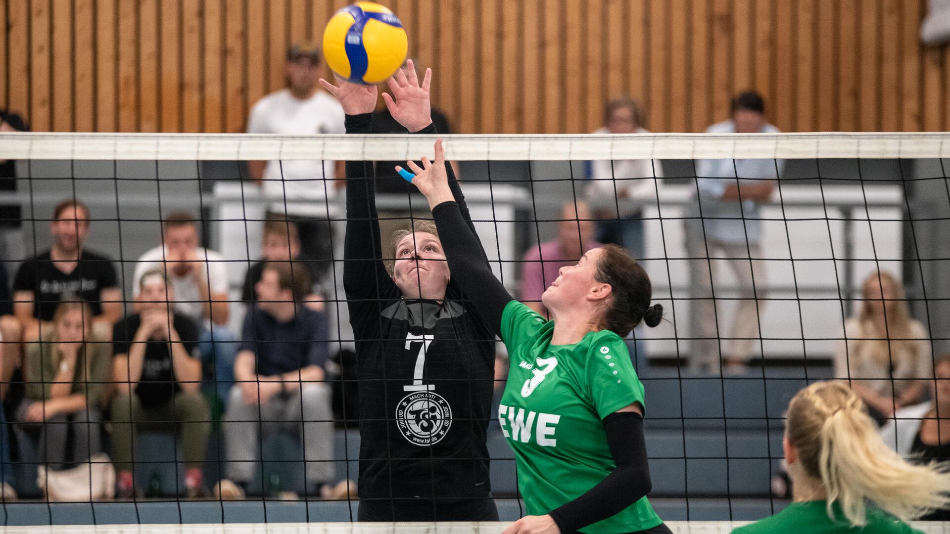 Zwei Frauen springen an einem Netz zu einem Ball hoch.