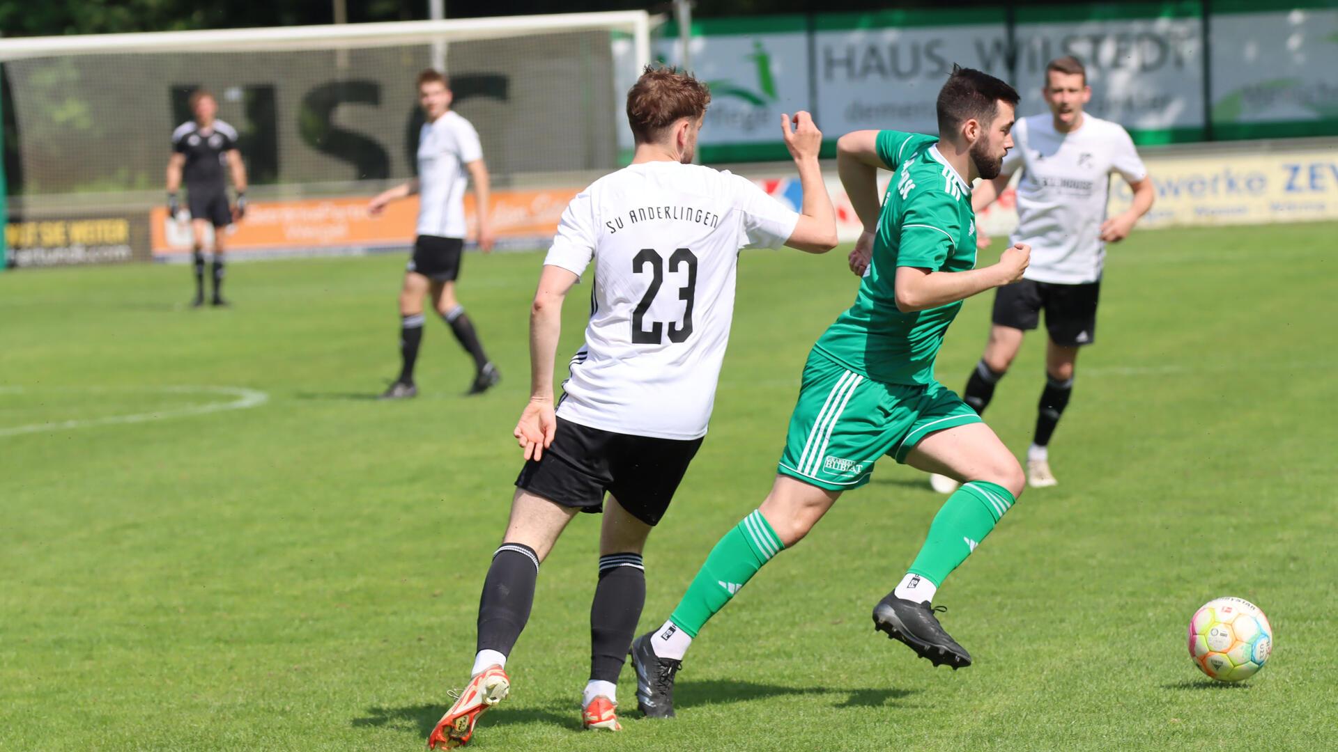 drei Männer in schwarzweißen Trikots und ein Mann im grünen Trikotspielen Fußball