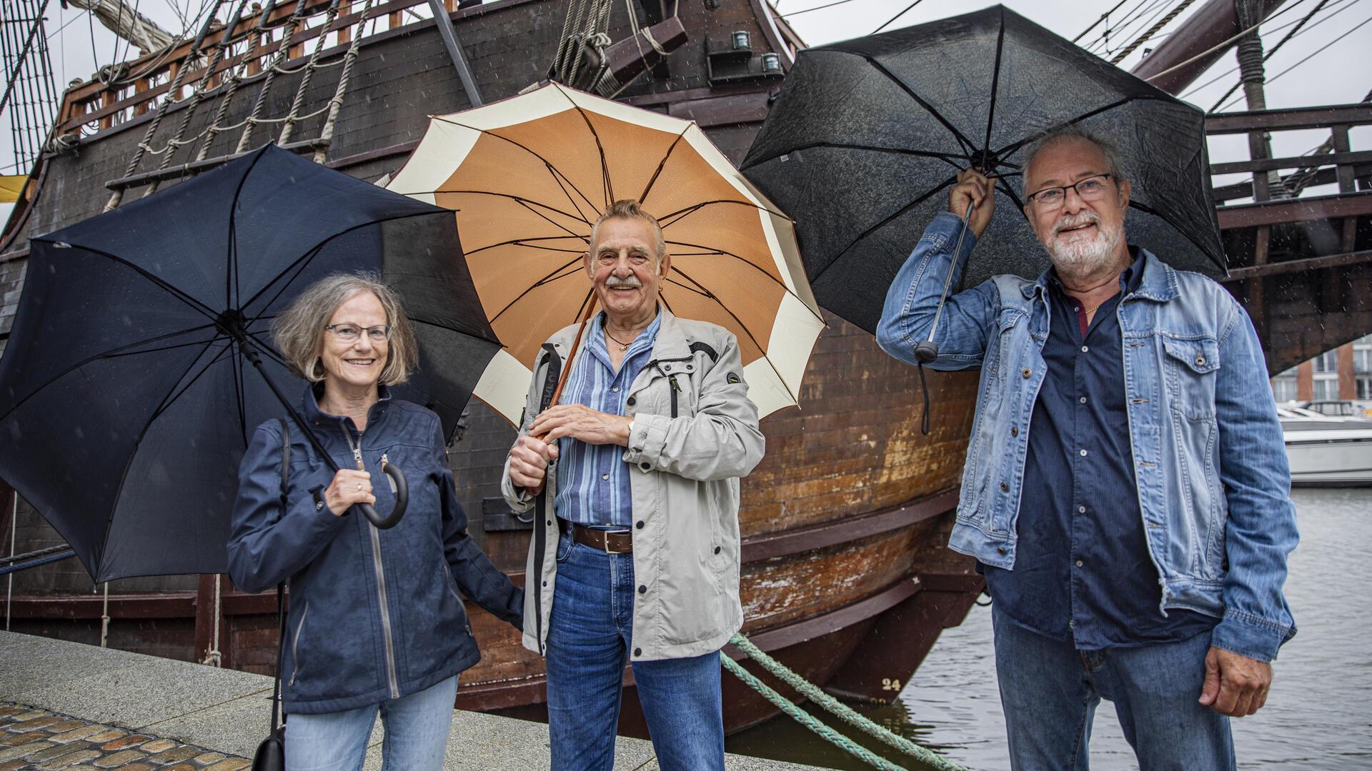 Drei Menschen im Regen mit Regenschirmen. 