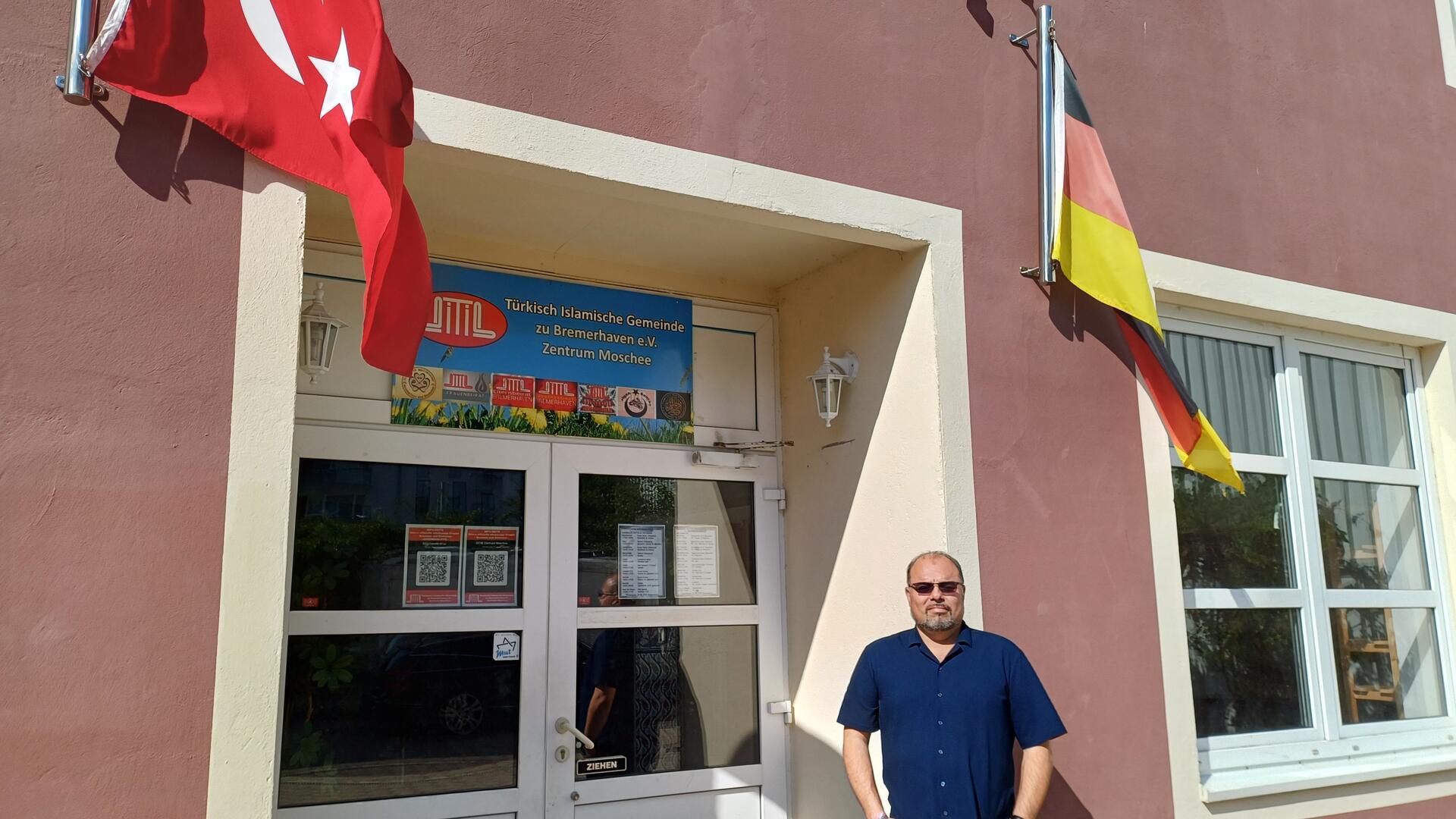 Ein Mann vor einem Eingang mit deutscher und türkischer Flagge.