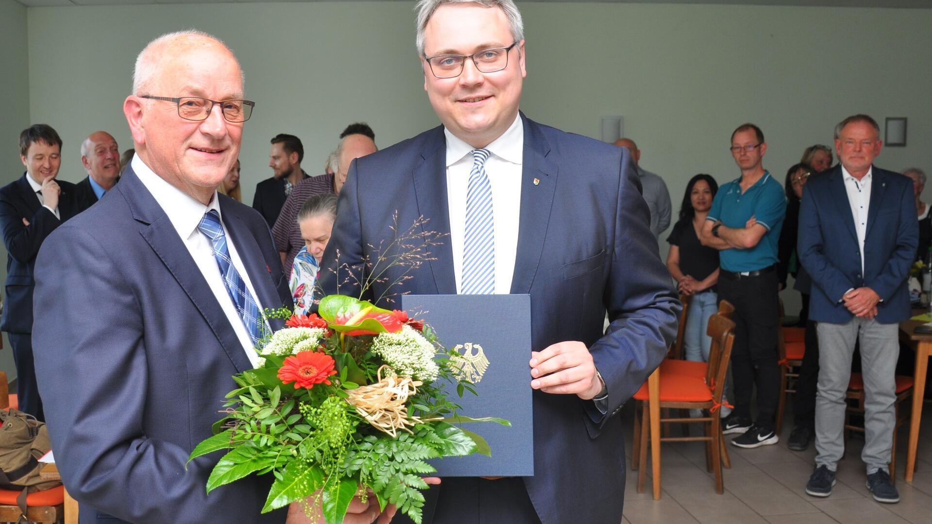 Feierlicher Moment: Während Landrat Marco Prietz den Verdienstorden der Bundesrepublik Deutschland und die vom Bundespräsidenten unterschriebene Urkunde an Arnold Renken (links) überreicht, erheben sich die Festgäste von ihren Plätzen.