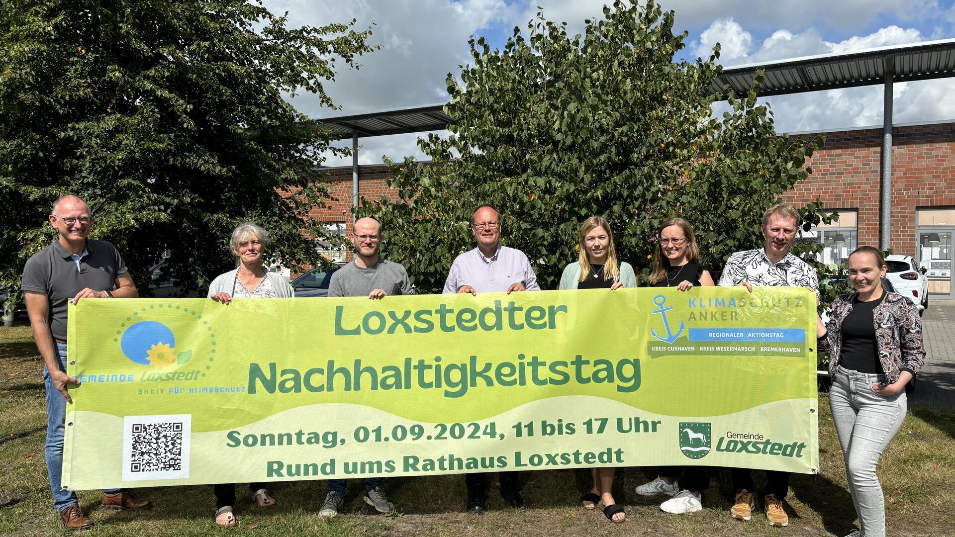 Acht Männer und Frauen halten ein Plakat mit der Aufschrift "Loxstedter Nachhaltigkeitstag" in die Kamera.