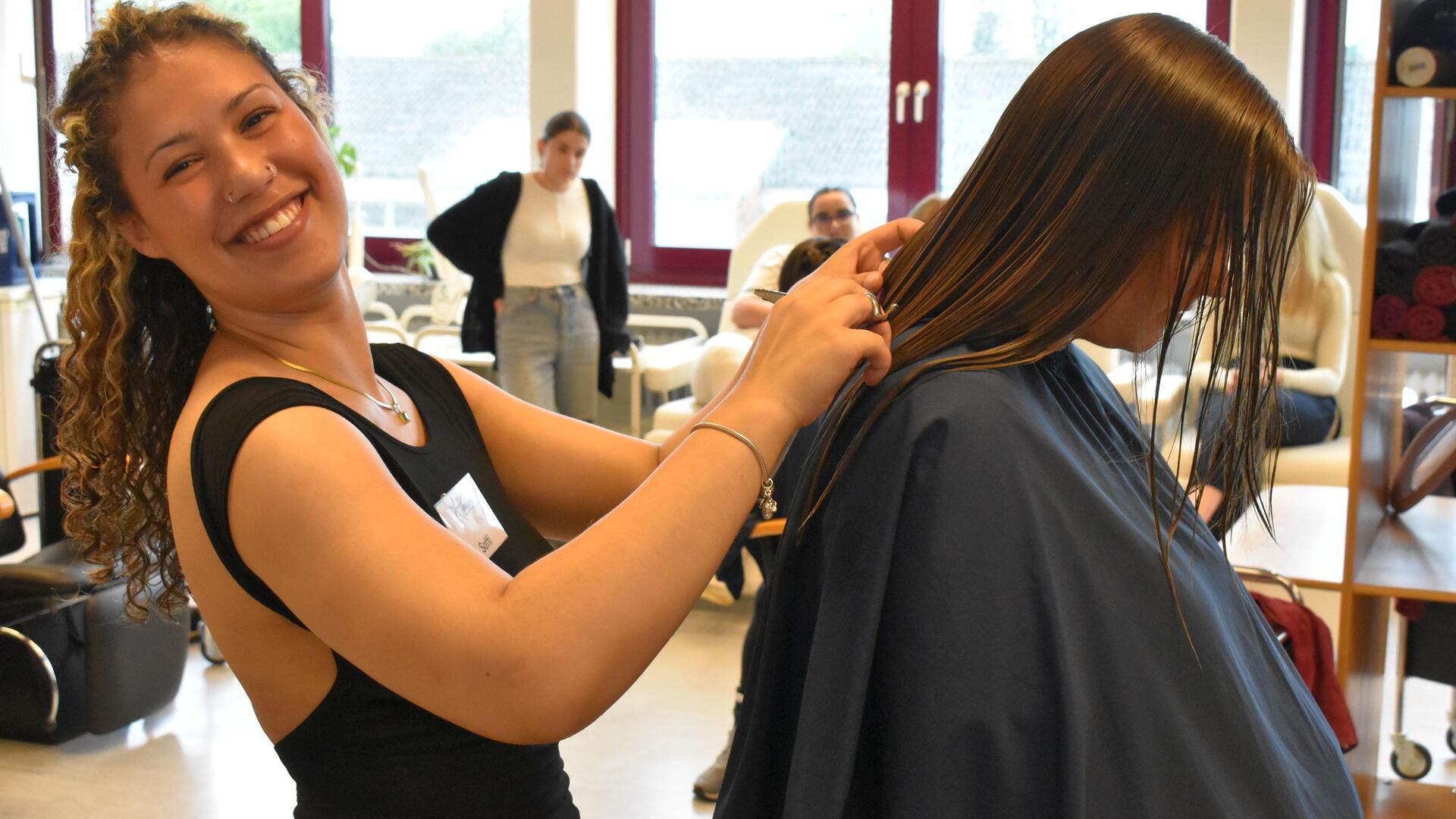 Eine junge Frau arbeitet als Friseurin und lächelt in die Kamera.