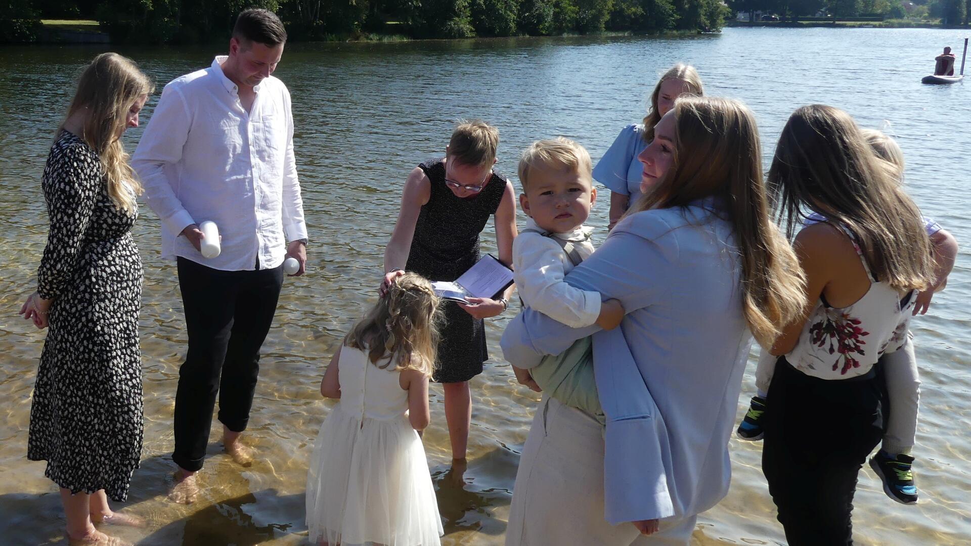 Eine Familie steht im Wasser im Uferbereich des Sieverner Sees, während ein junges Mädchen gerade mit Seewasser getauft wird.