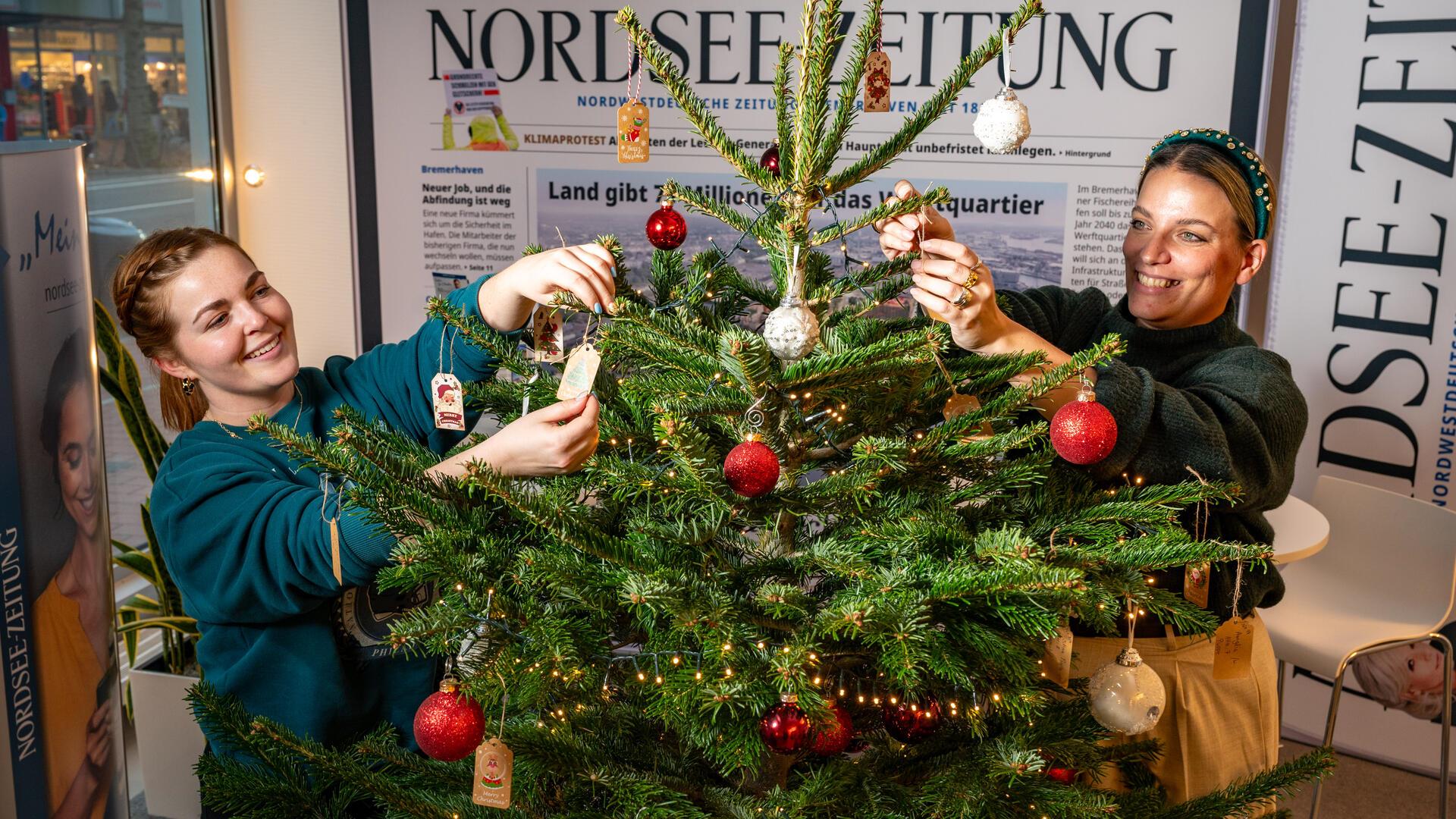 Zwei Frauen schmücken einen Tannenbaum mit Kugeln und Wunschzetteln.