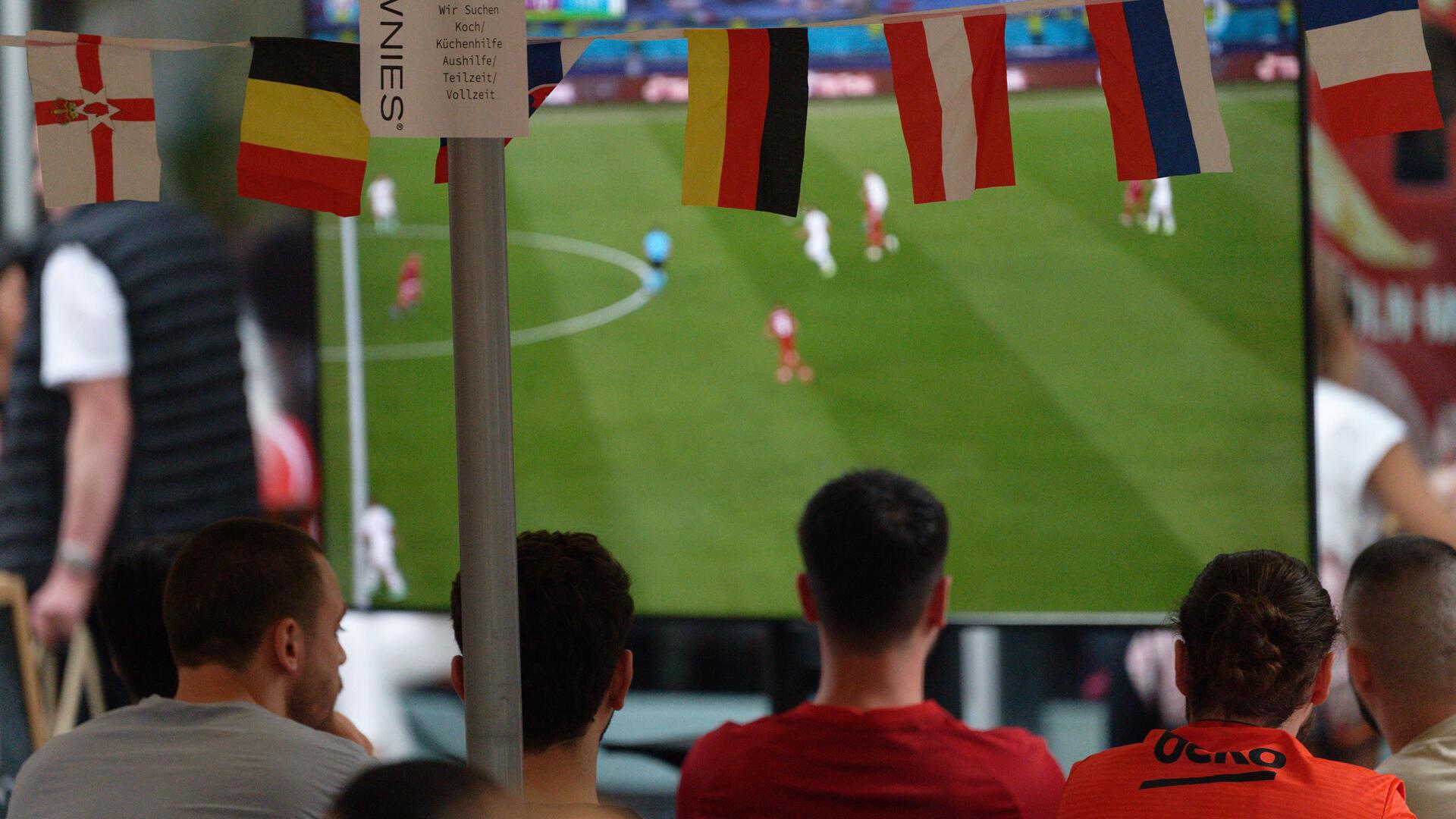 Menschen schauen sich auf einer Leinwand ein Fußballspiel an. 