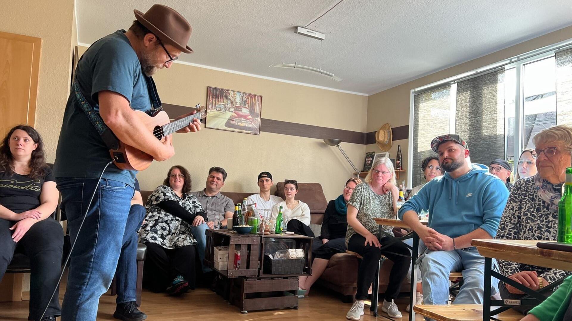 Gregor Meyle spielt Gitarre in einem Wohnzimmer vor Zuschauern.