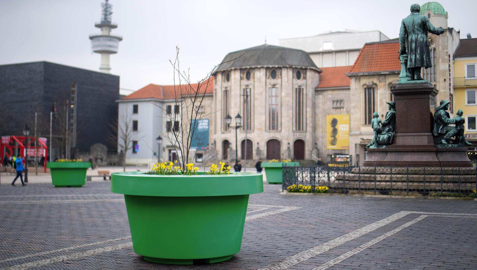 Ein grüner Kübel ist auf einem öffentlichen Platz zu sehen. 