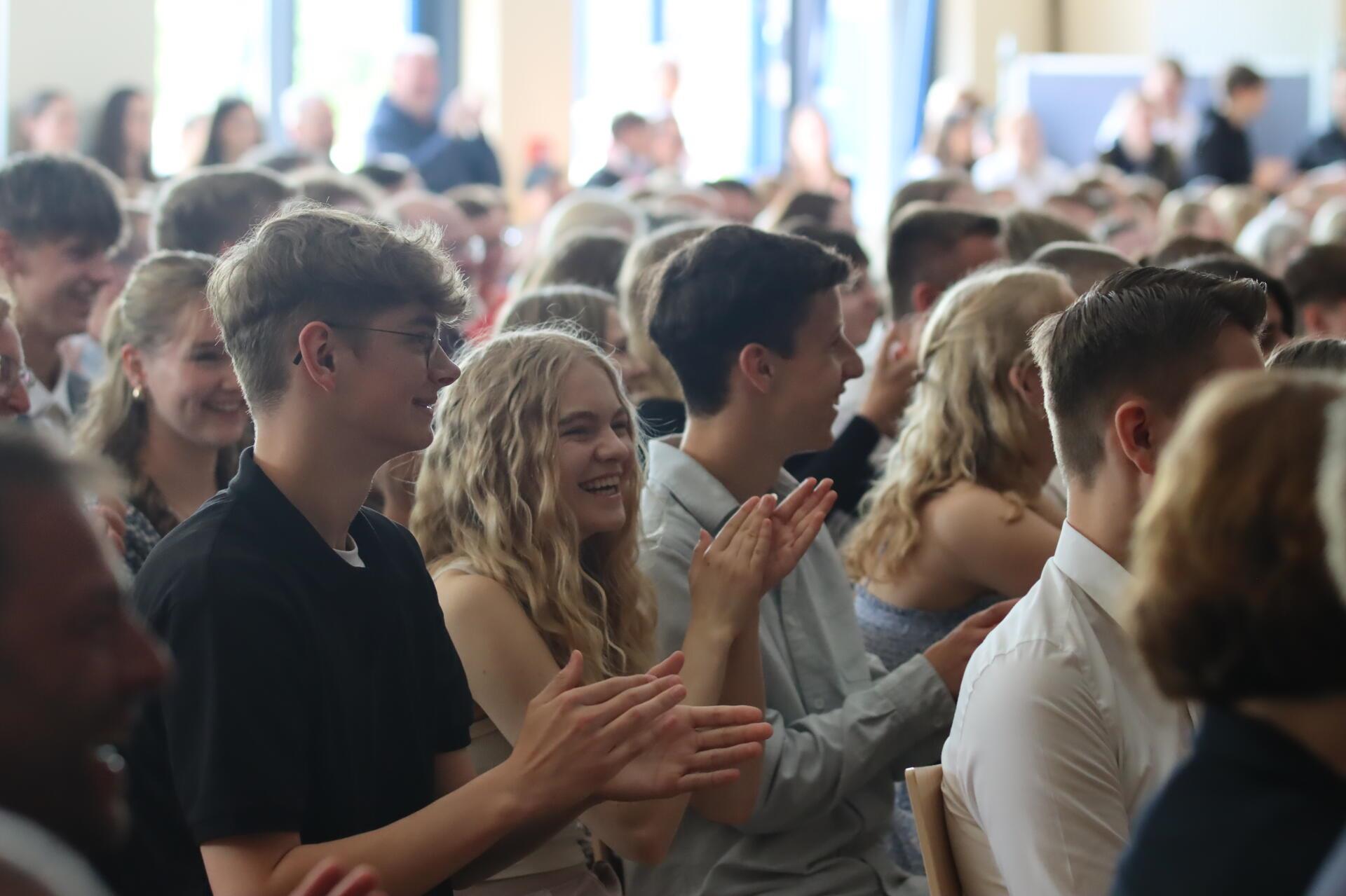 Junge Menschen sitzen dicht an dicht, lachen und klatschen in die Hände.