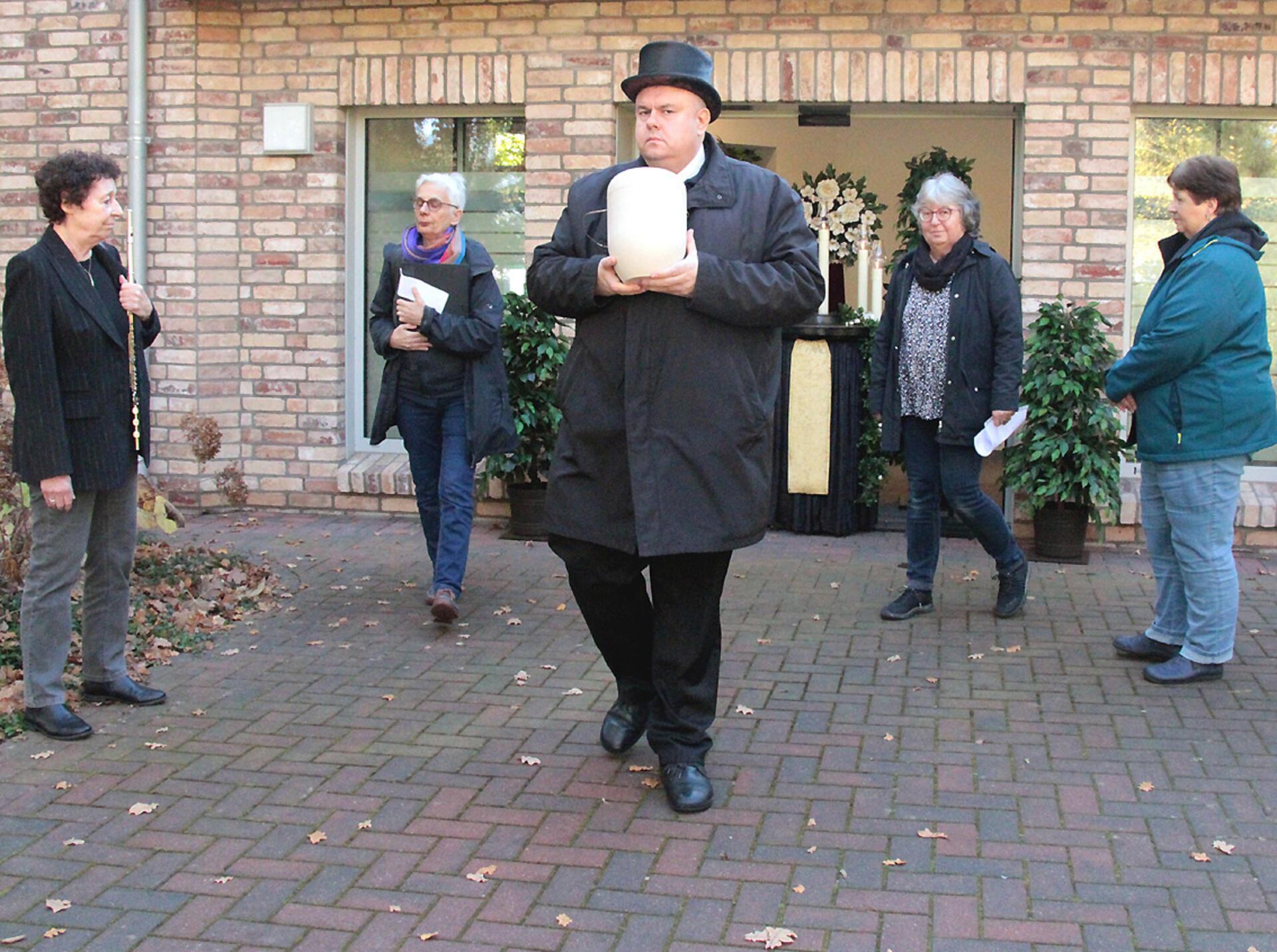 Mehrere Menschen vor einer Kapelle Bestatter mit Urne in der Hand