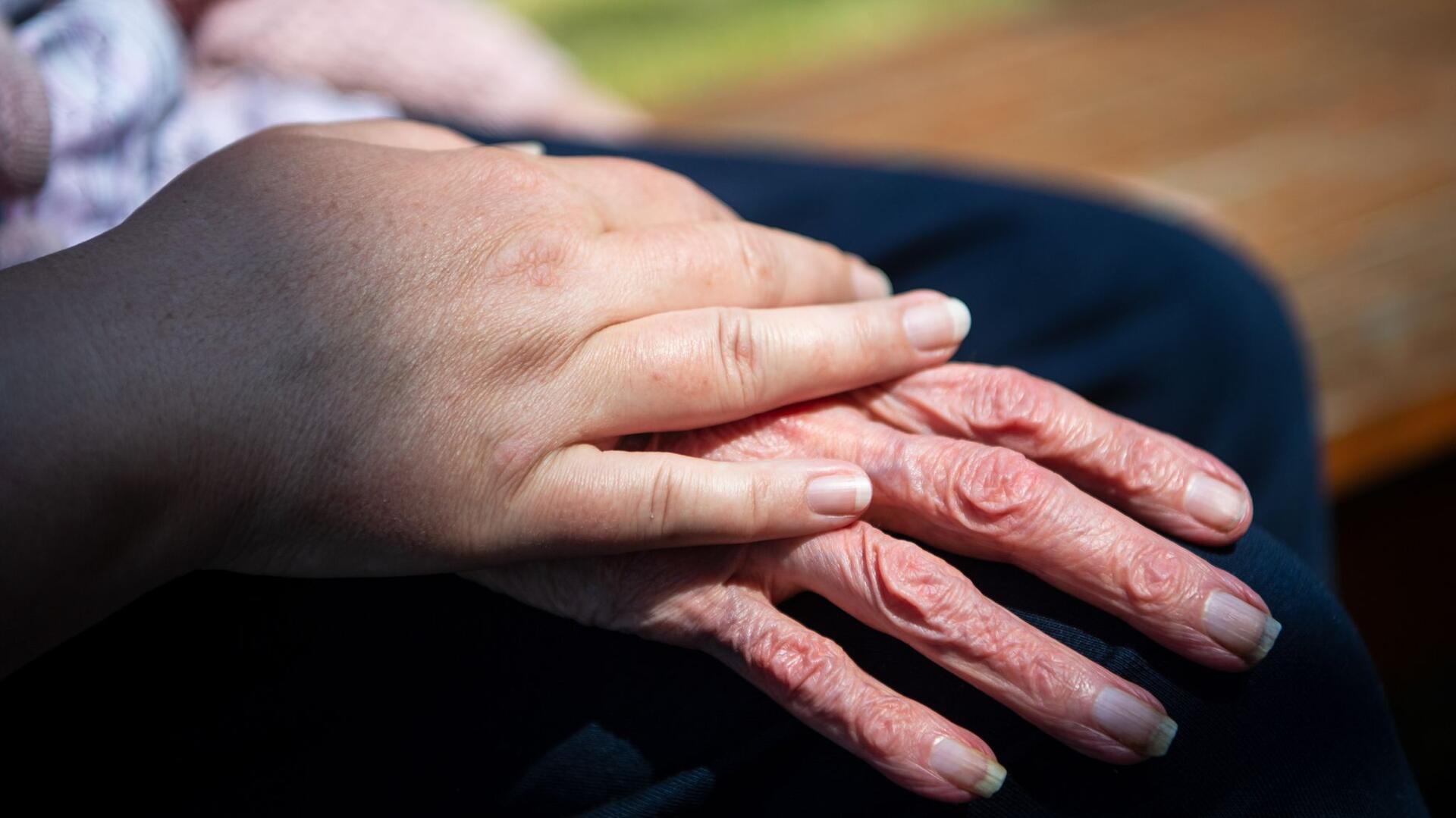 Eine Pflegekraft hält die Hand eines Pflegebedürftigen. 