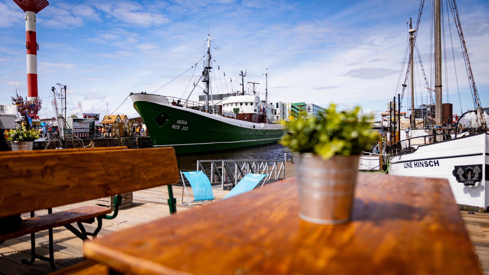 Ein Blick über einen Tisch auf Schiffe, die im Hafen liegen. Die Sonne scheint.